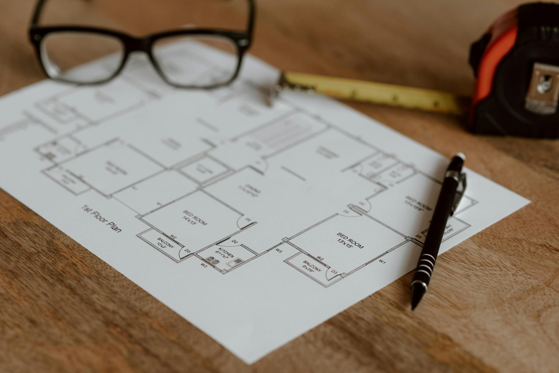 Floor plan sketch on a wooden table with eyeglasses, a pen, and a tape measure nearby.