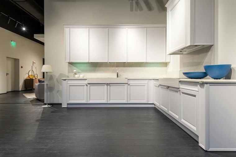 Modern white kitchen display with cabinets, dark flooring, and blue bowls on the counter