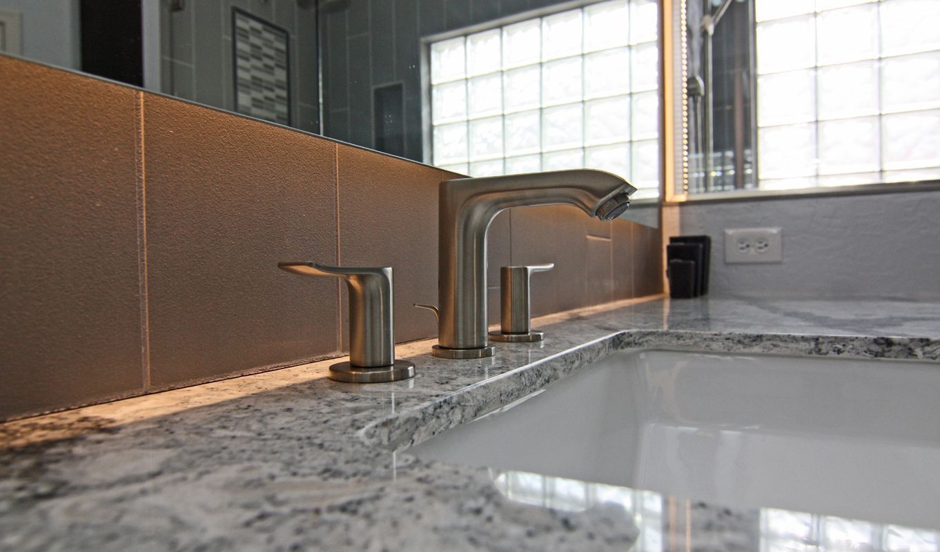 Chrome bathroom faucet on a marble sink with a tiled backsplash and window light