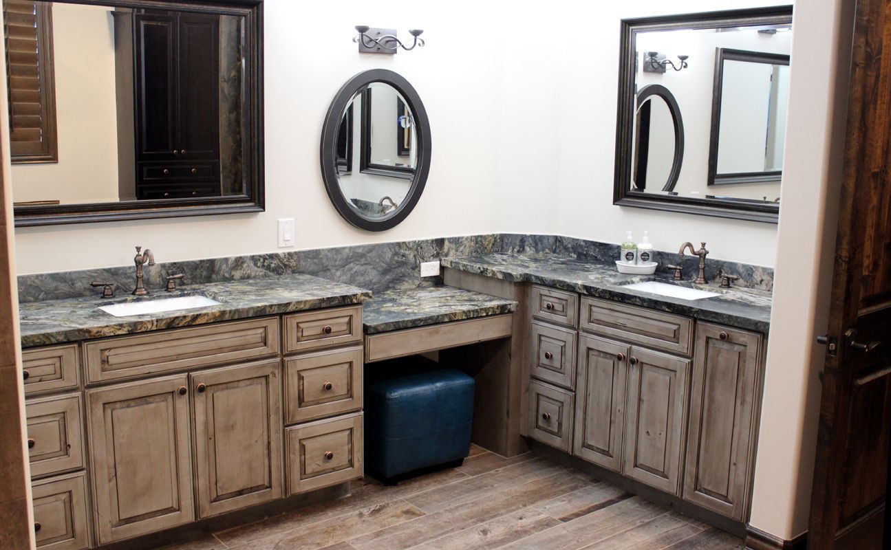 Bathroom vanity with double sinks, granite countertop, wood cabinets, and mirrors