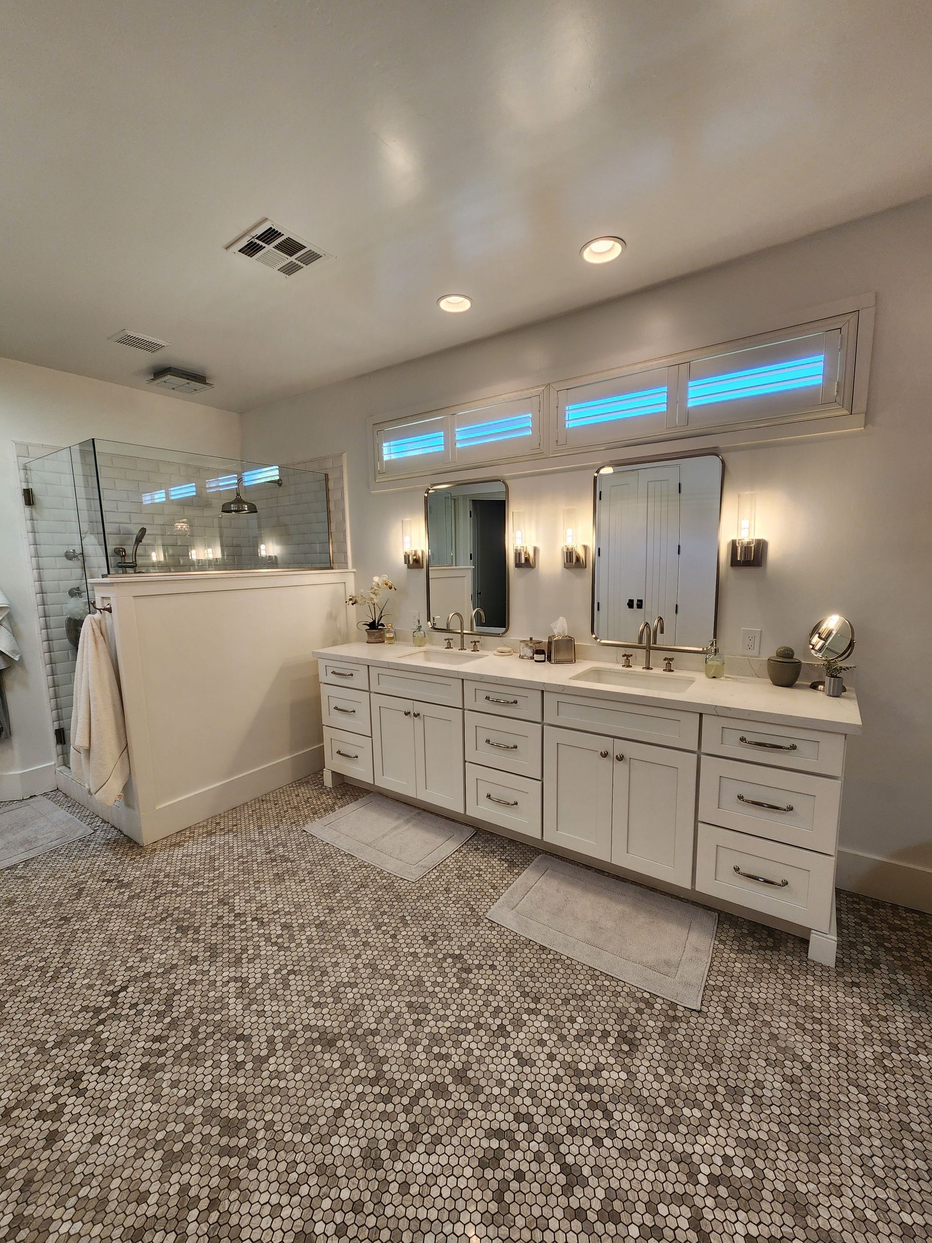 Bright bathroom with double vanity, large mirror, and patterned floor rug.
