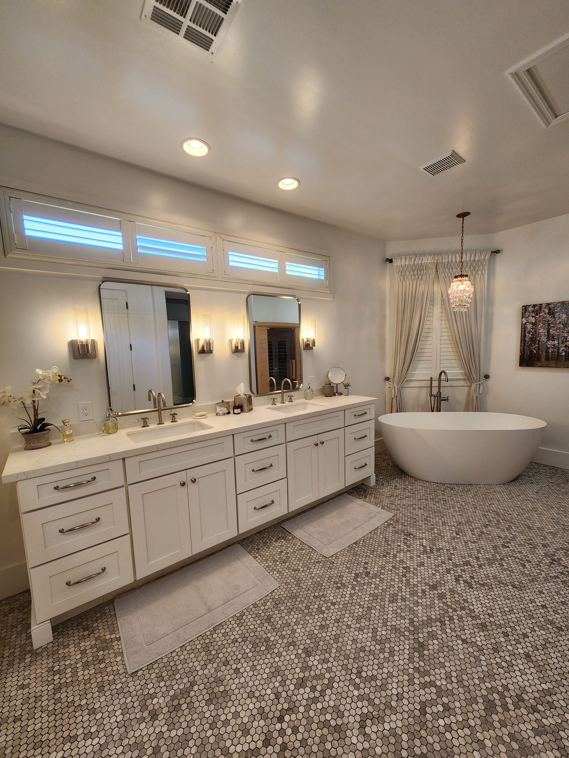 Bright spa-style bathroom with double vanity, large mirrors, freestanding tub, and patterned tile floor.