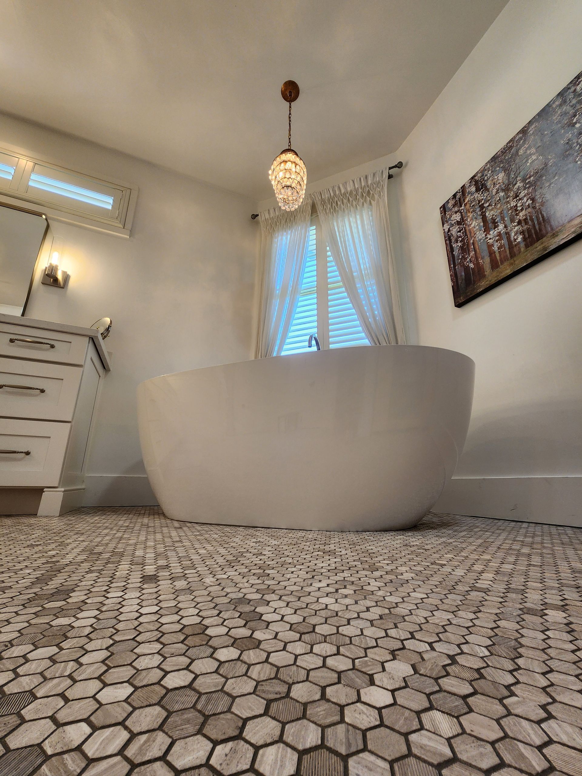 Modern bathroom with freestanding white tub, mosaic tile floor, and window light