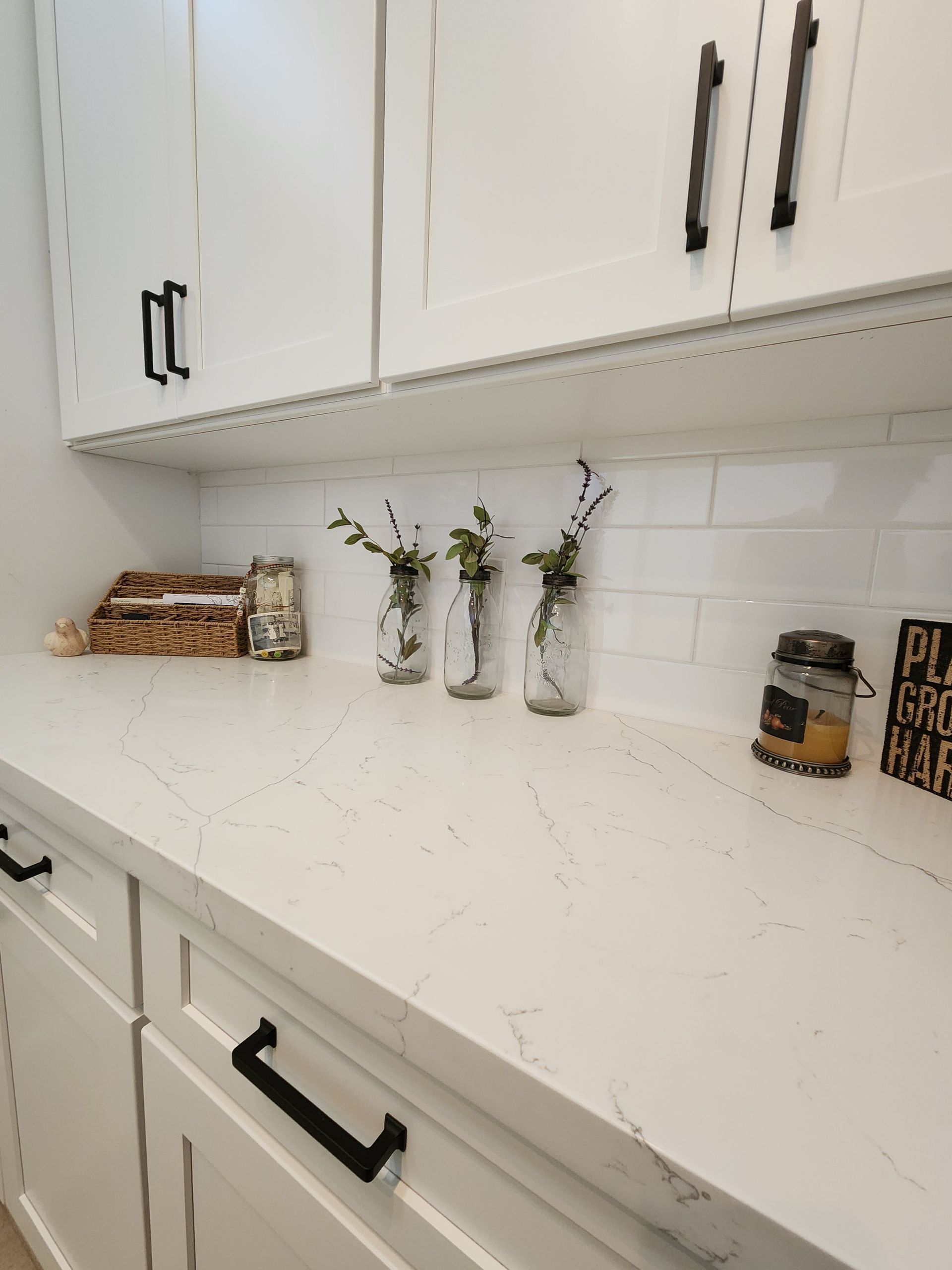 White kitchen countertop with decorative vases, a basket, and jars beneath white cabinets