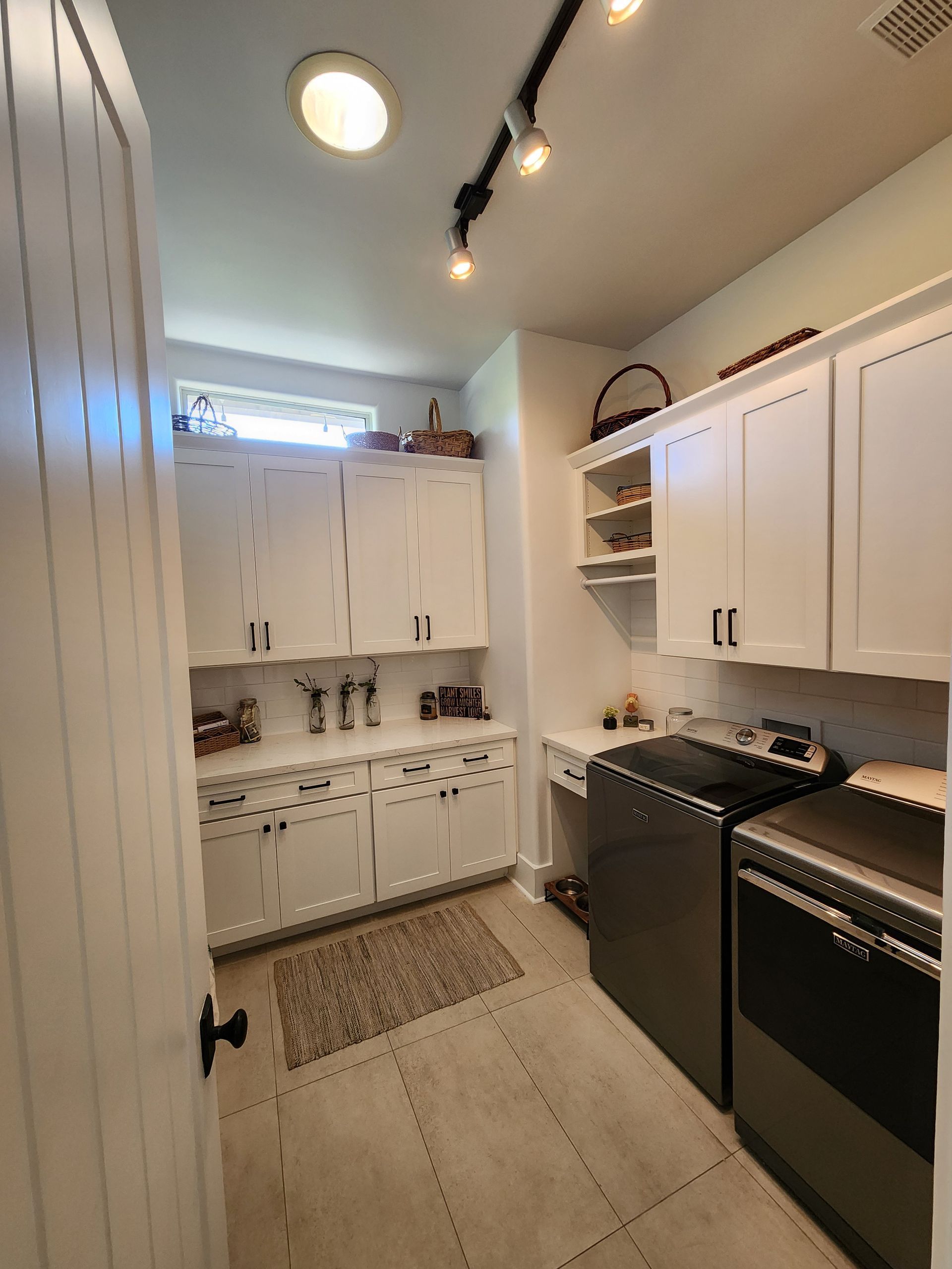 Narrow white kitchen with cabinets, black stove and dishwasher, and a window above the sink.