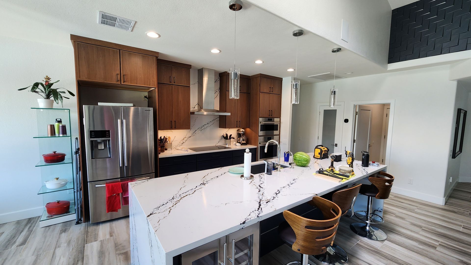 Modern kitchen with white island, stainless fridge, wooden cabinets, and bar stools under pendant lights