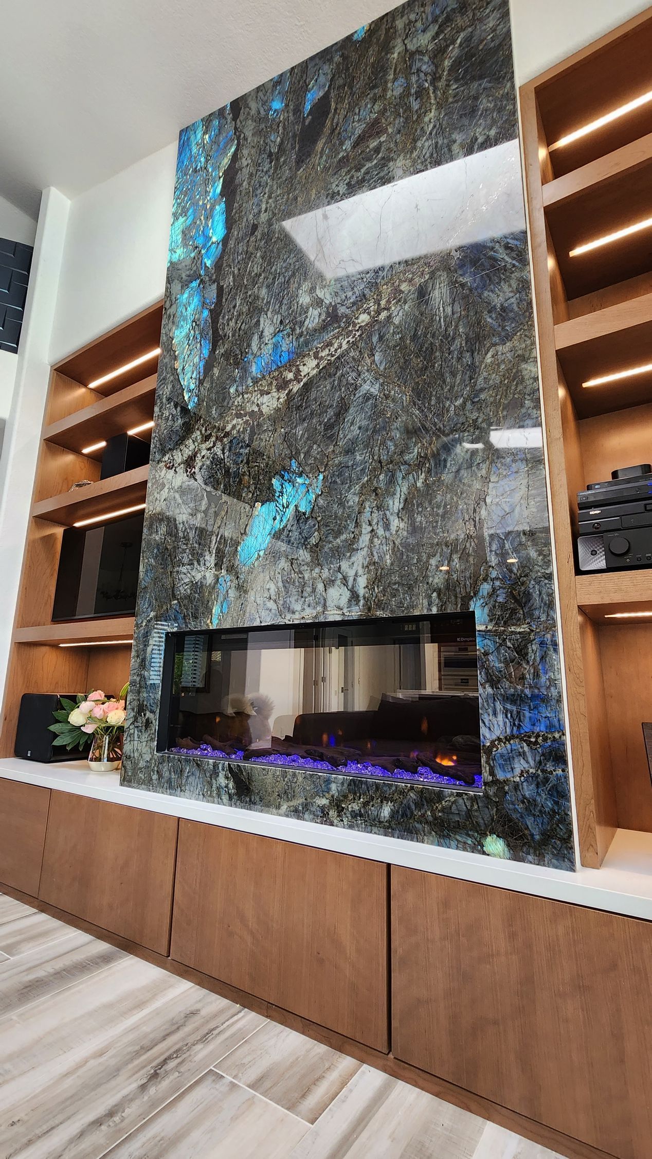 Modern living room with a tall blue-and-gray stone fireplace, built-in shelves, and wood cabinets