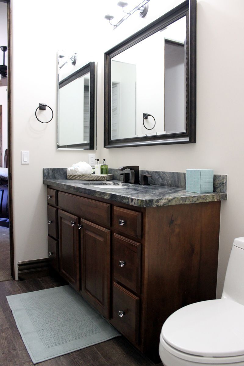 Bathroom vanity with dark wood cabinets, granite countertop, mirrors, and a white toilet on the right
