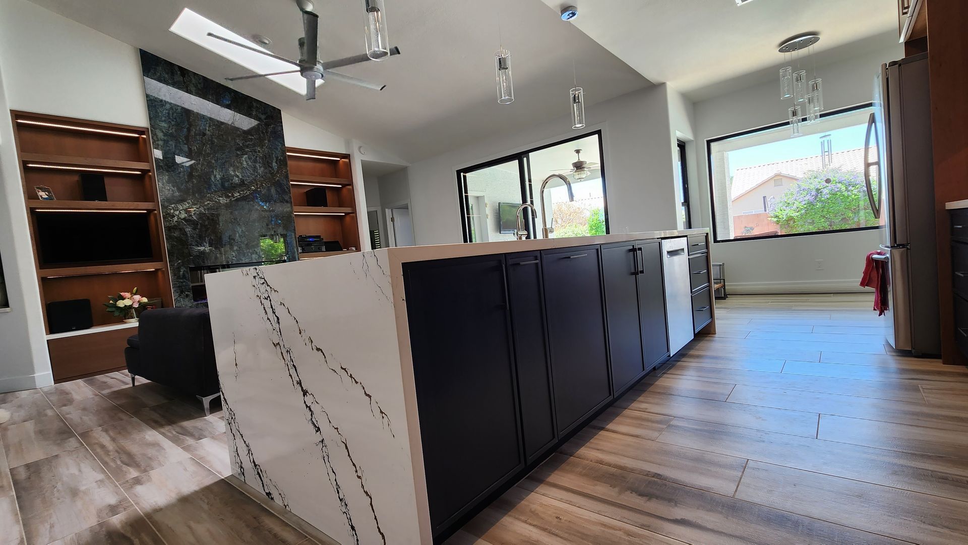 Modern kitchen with dark cabinets, marble island, and large windows overlooking greenery