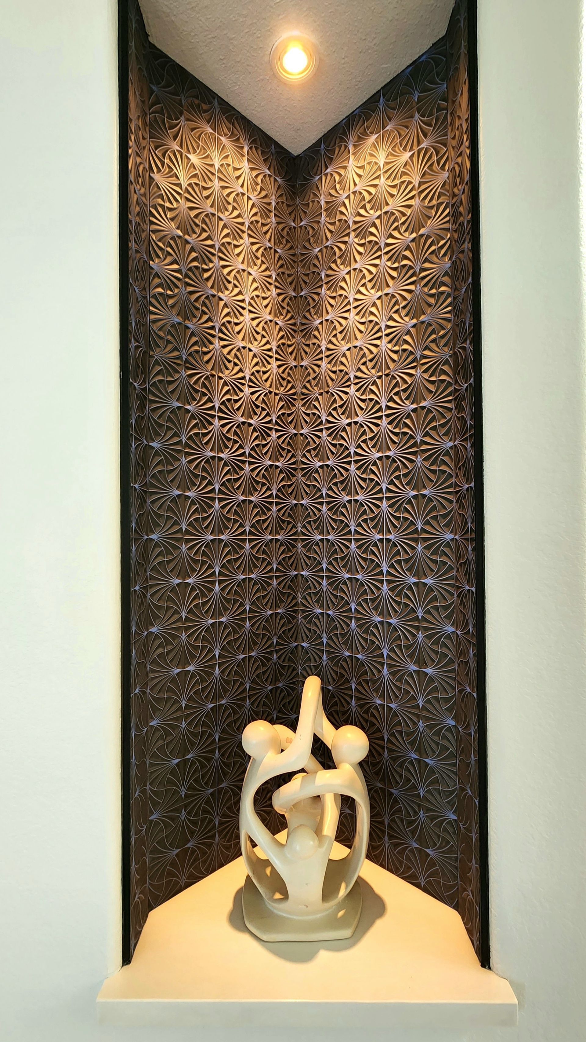 Abstract sculpture in a recessed alcove with dark textured walls and a spotlight overhead