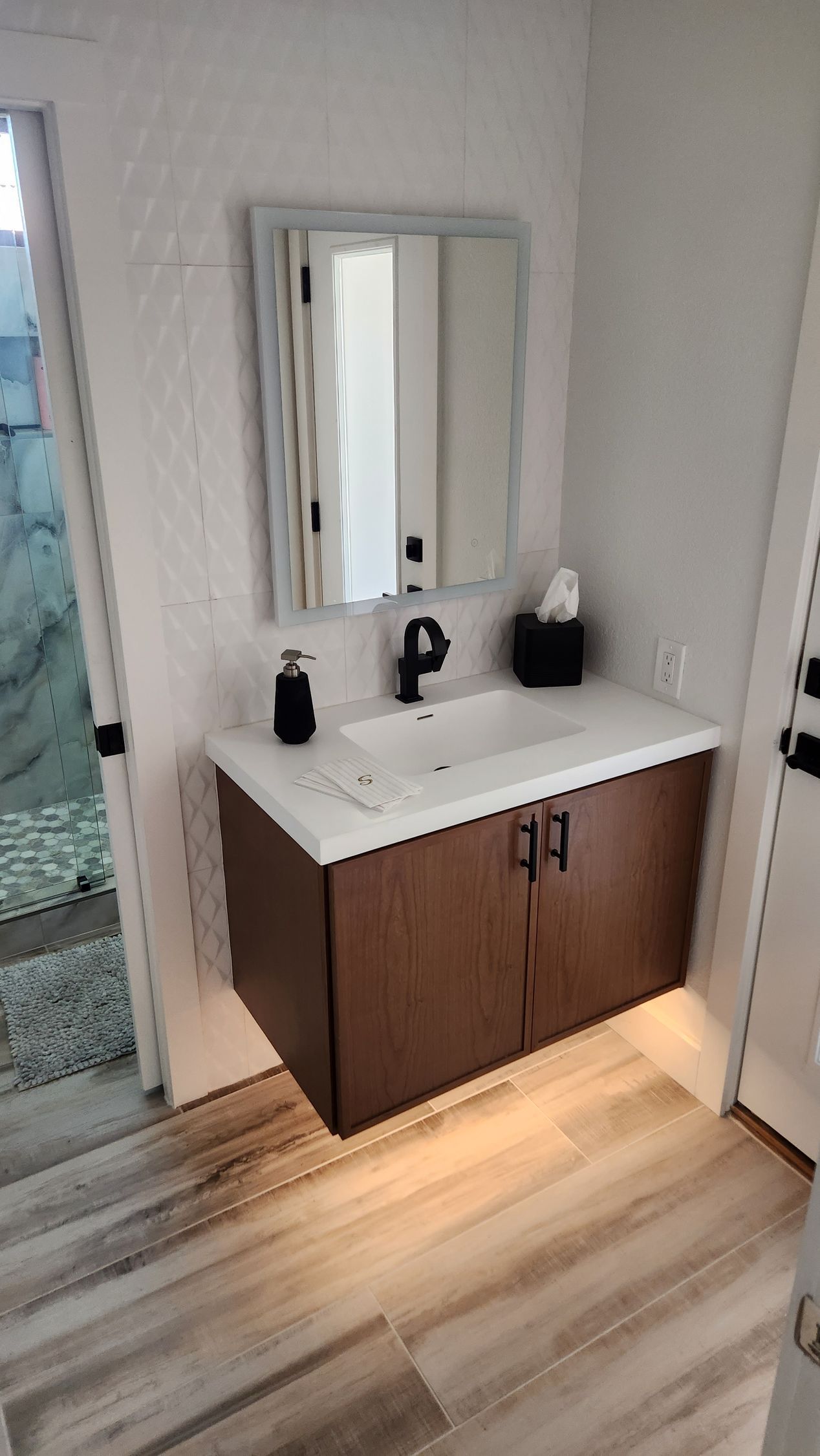 Modern bathroom vanity with mirror, white sink, brown cabinet, and soft lighting on wood-look floor.