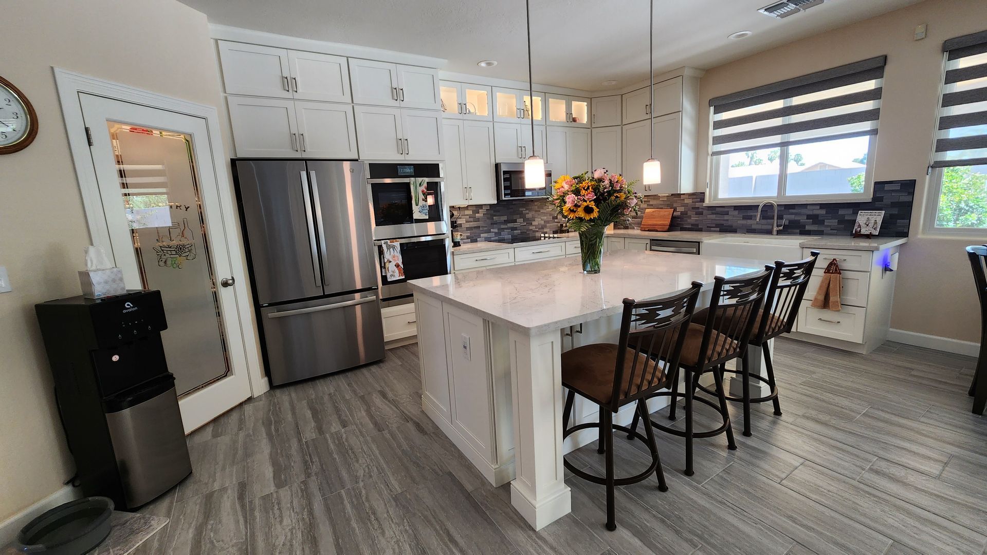 Modern kitchen with stainless steel appliances, white island, dark bar stools, and large window view