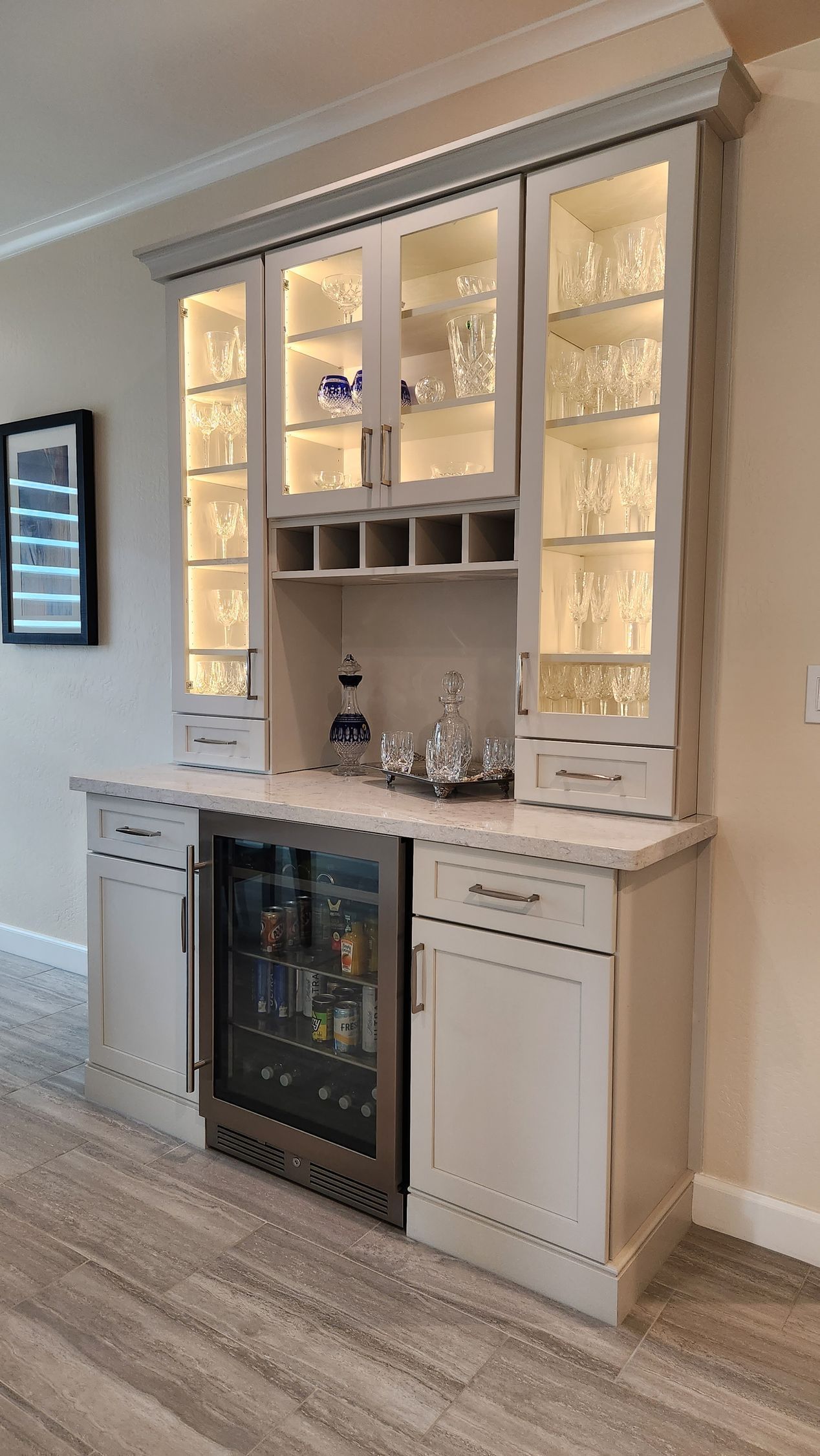 Built-in home bar cabinet with glass shelves, mirror backing, wine cooler, and light wood finish