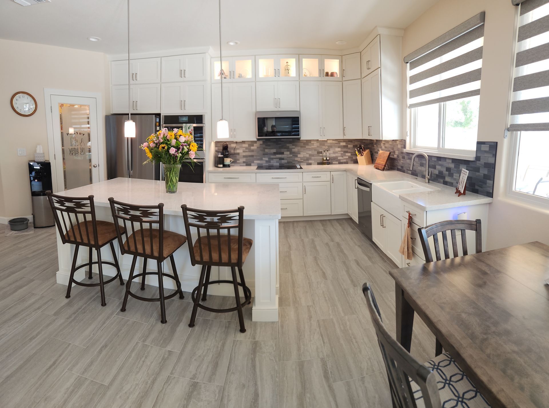 Bright white kitchen with island, bar stools, pendant lights, and large windows; dining table in foreground