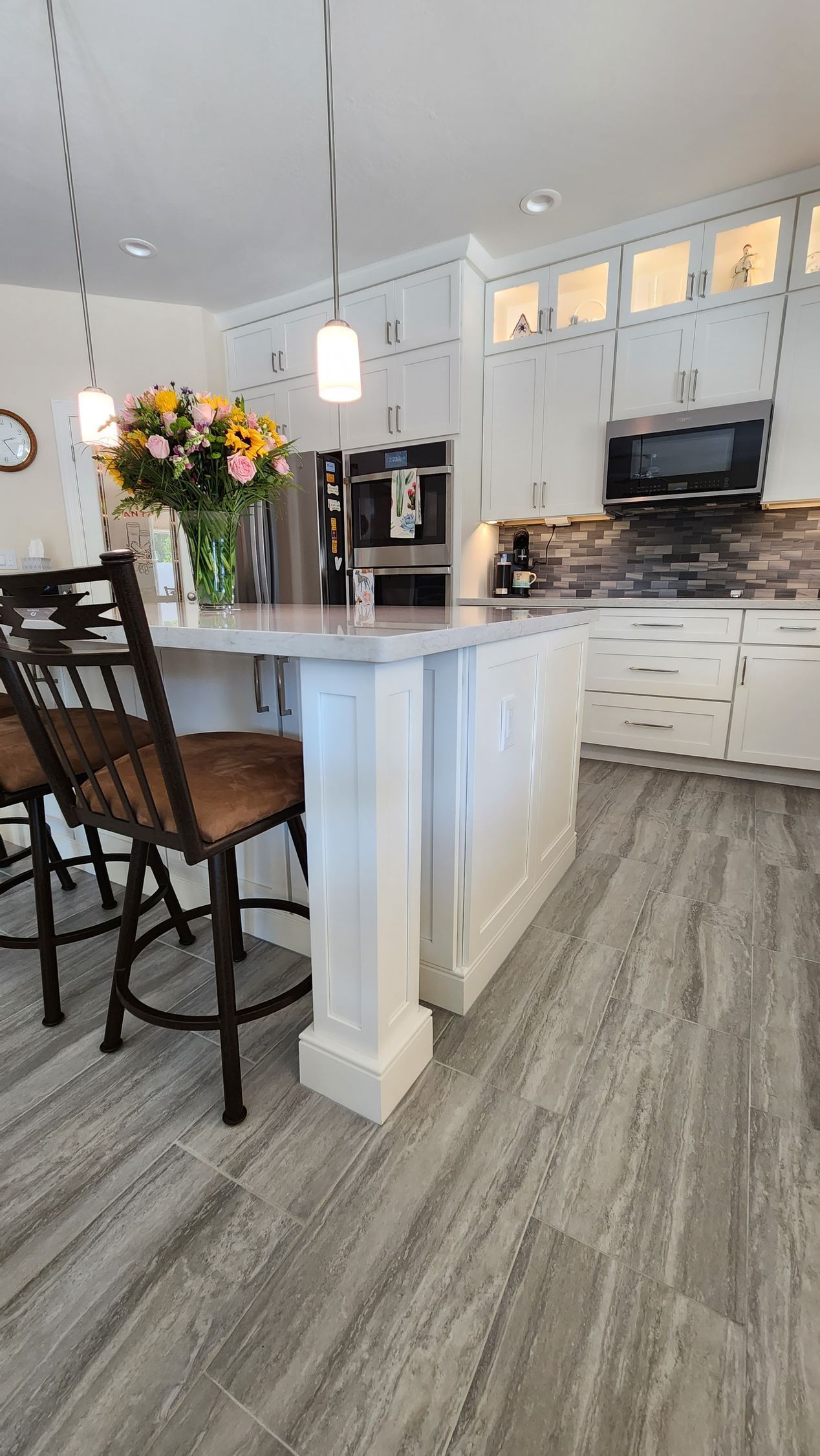 Bright kitchen with island, barstools, flowers, and gray wood-look flooring