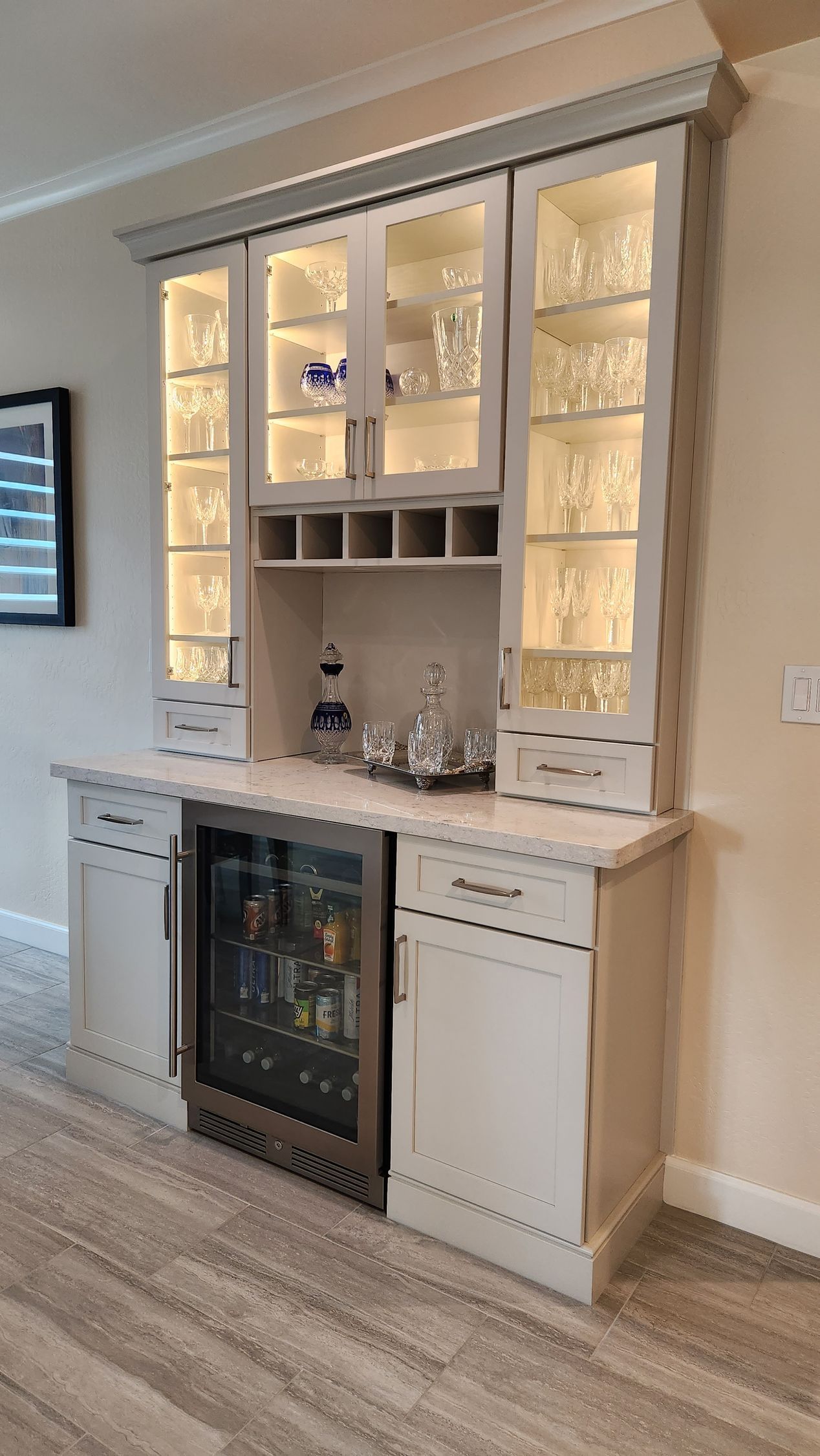 Built-in home bar cabinet with glassware, white cabinetry, and a small wine fridge against a beige wall.