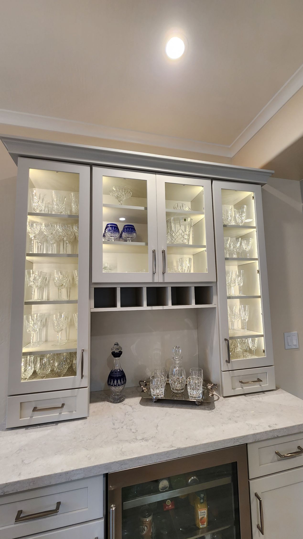 White kitchen cabinets with glass doors and built-in wine cooler under a bright ceiling light