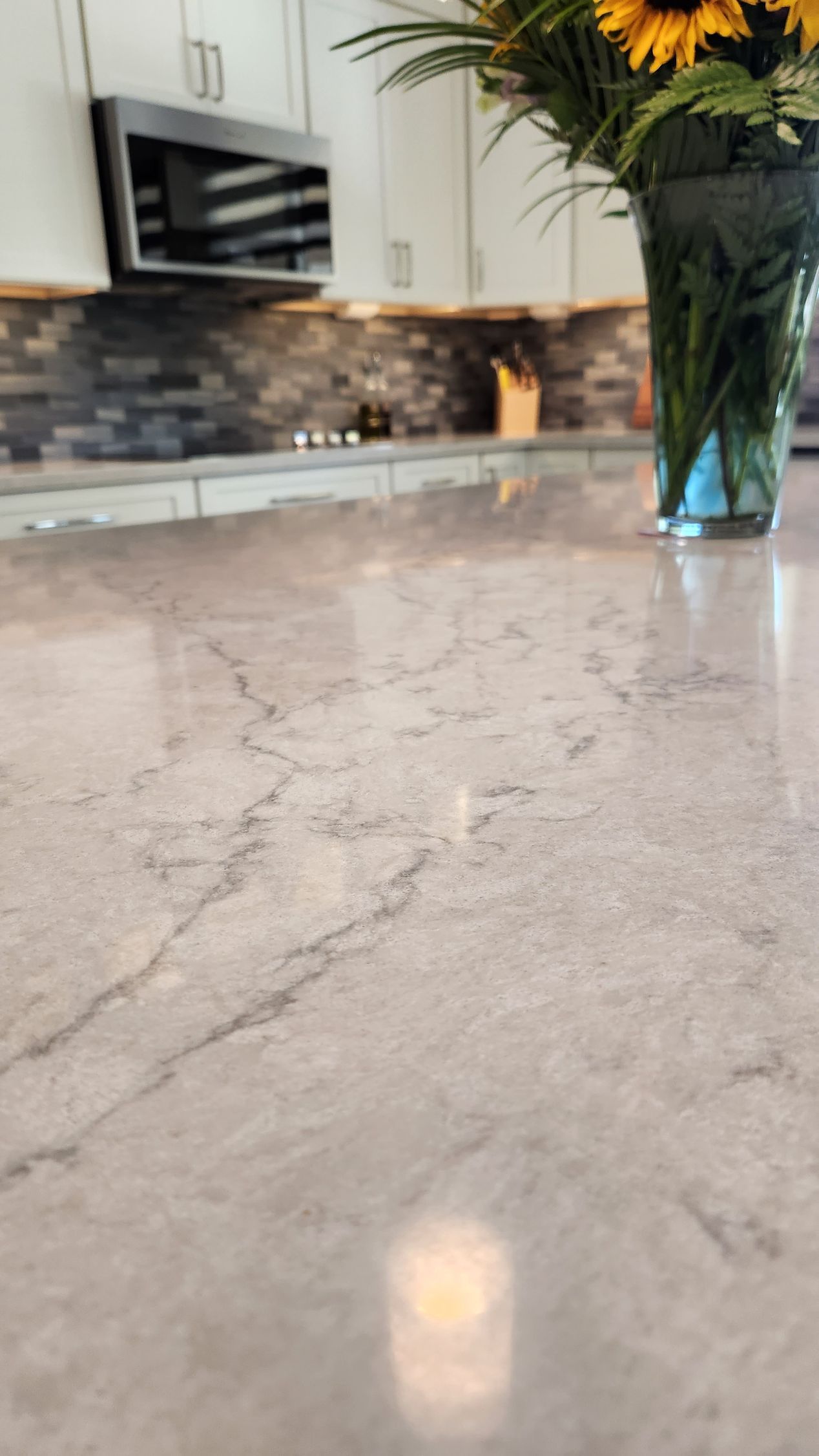 Kitchen counter with marble surface, blurred backsplash, and a vase of yellow flowers on the right.