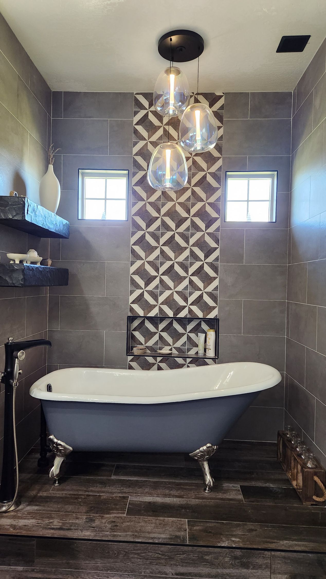 Narrow bathroom with a clawfoot tub, patterned tile wall, pendant light, and two small windows.