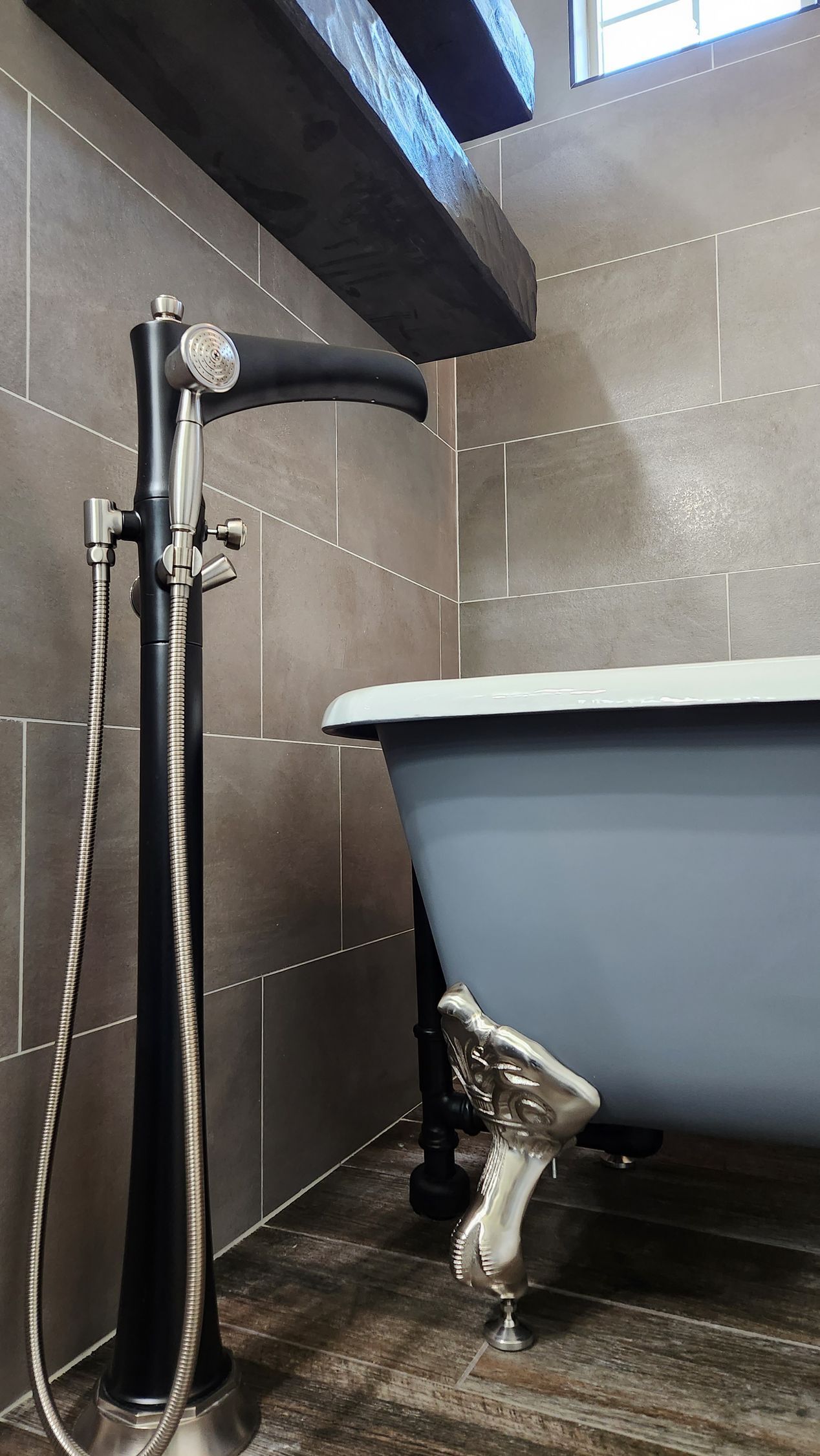 Small bathroom with a gray bathtub and exposed plumbing against tiled walls.