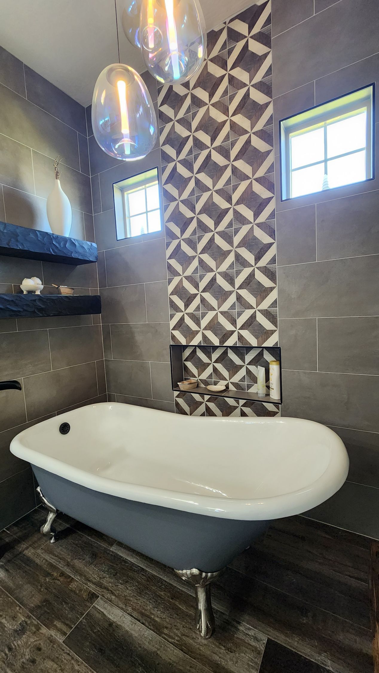 Modern bathroom with freestanding white tub, patterned tile accent wall, gray tiles, and pendant lights