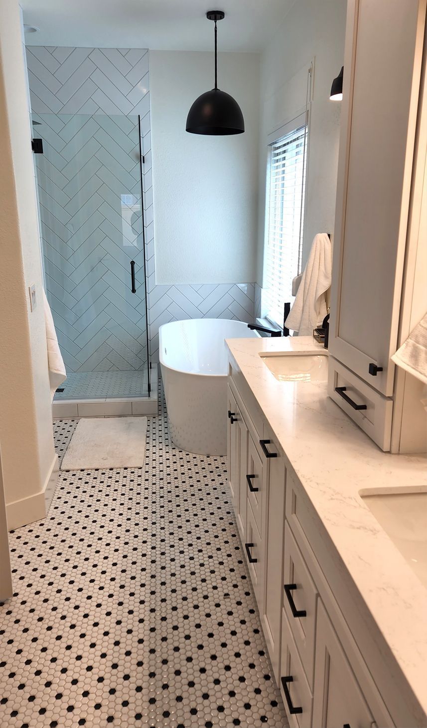 Narrow white bathroom with black-and-white tile floor, vanity, tub, and frosted glass shower door.