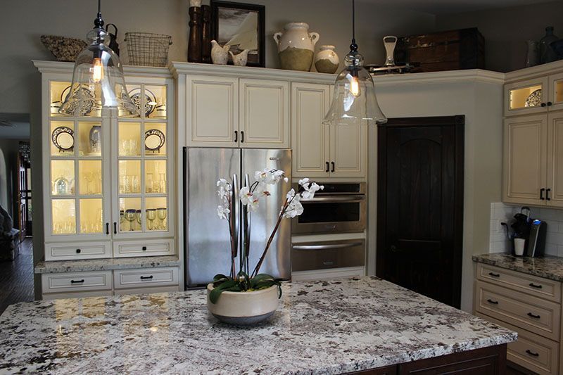 Modern kitchen with granite island, white cabinets, glass display cabinets, and hanging pendant lights.