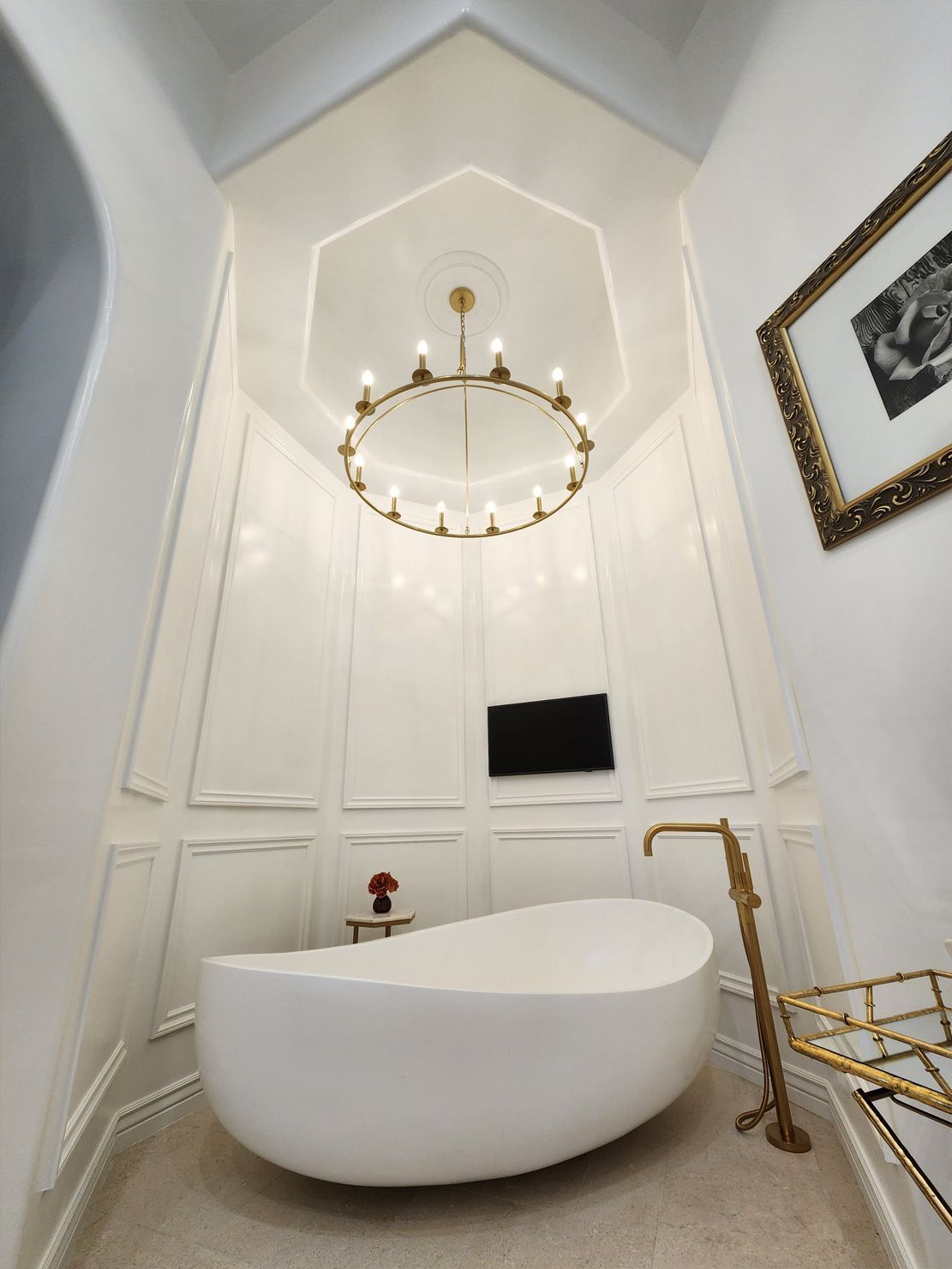 Bright white luxury bathroom with a freestanding oval tub, gold chandelier, and framed wall art