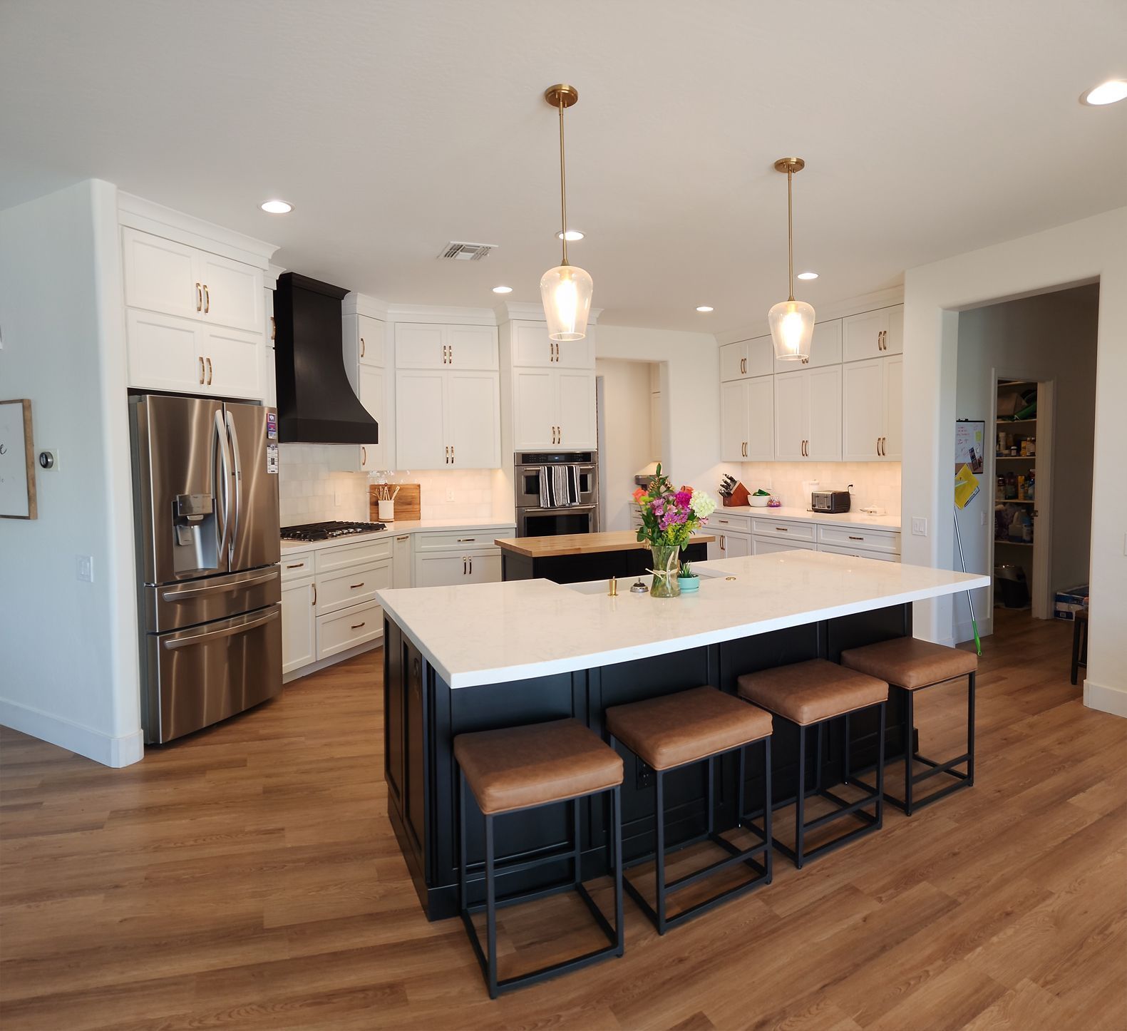 Bright modern kitchen with white cabinets, stainless appliances, wood floor, and a large island with stools