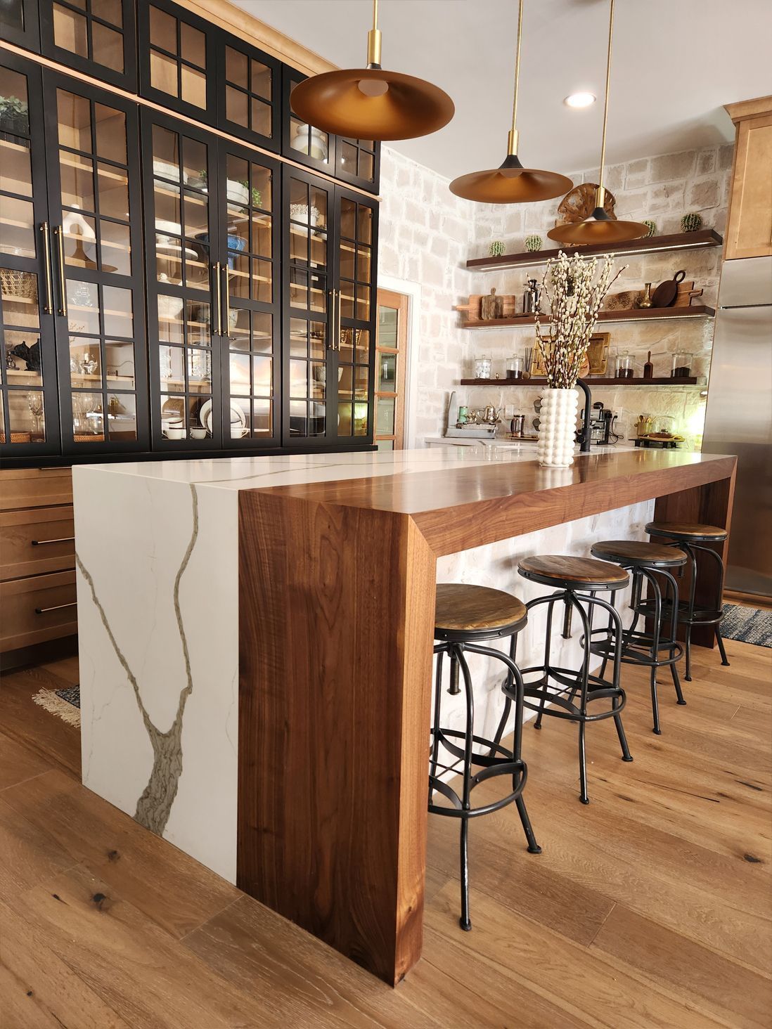 Modern kitchen with wood island, black stools, glass-front cabinets, and pendant lights
