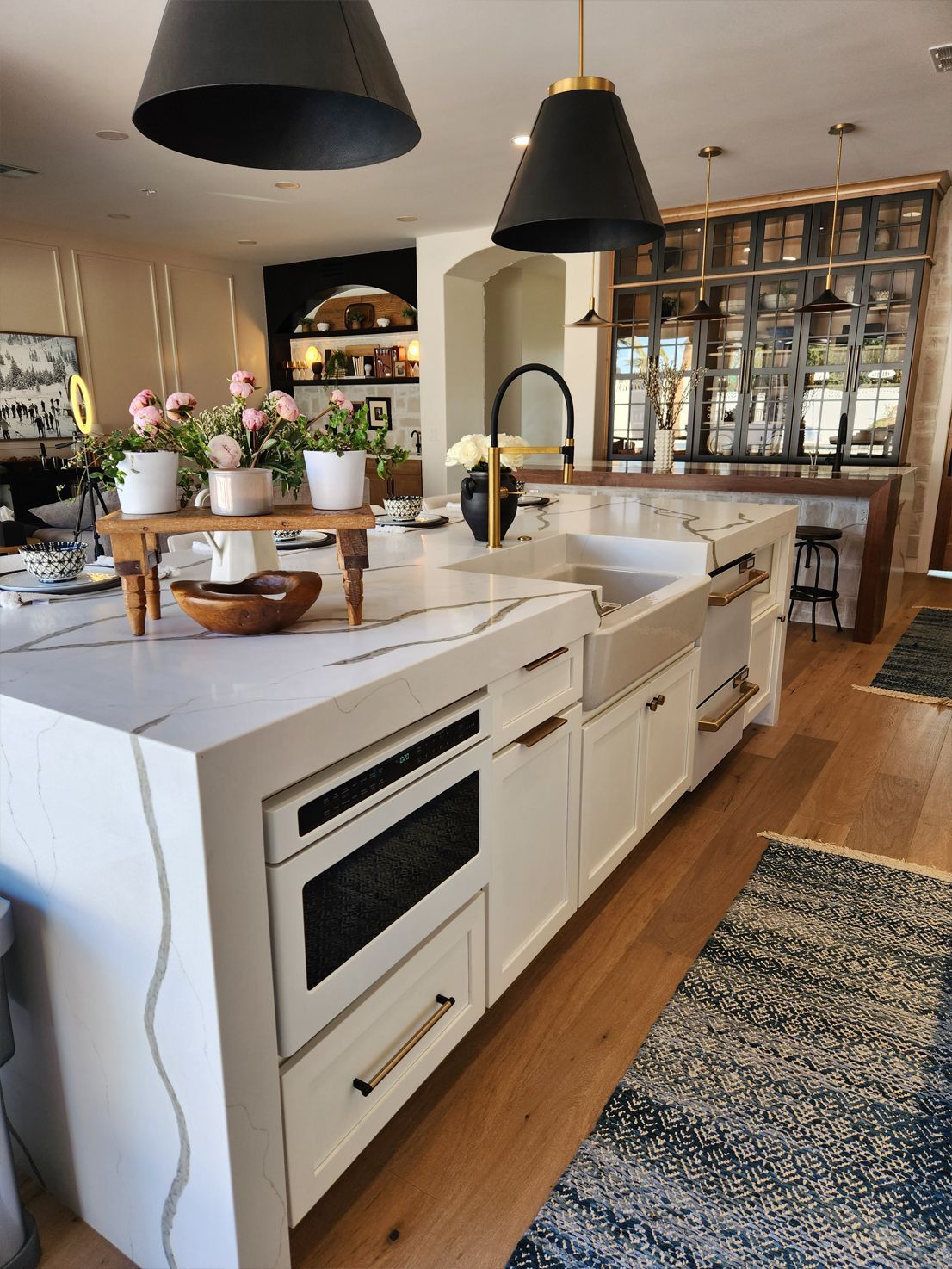 Bright modern kitchen with white island, black pendant lights, wooden floors, and flowers on the counter