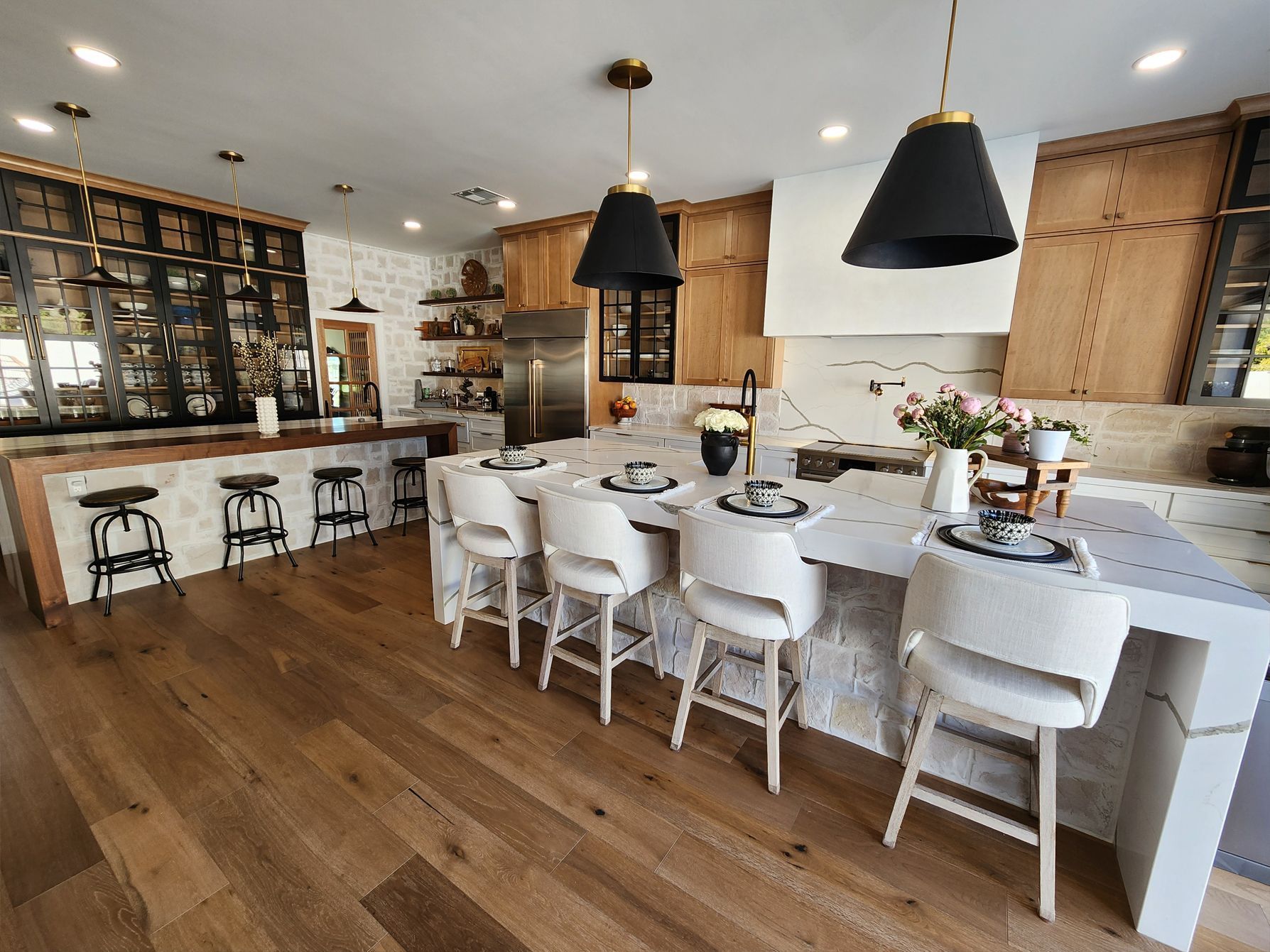 Modern white kitchen and dining area with large island, black pendant lights, and wooden floors