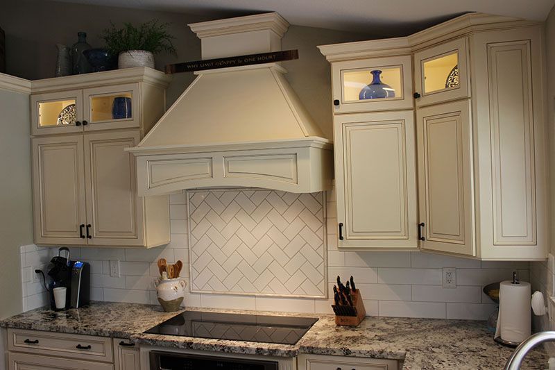 Cream kitchen with white cabinets, granite counter, and white tile backsplash surrounding a range hood.