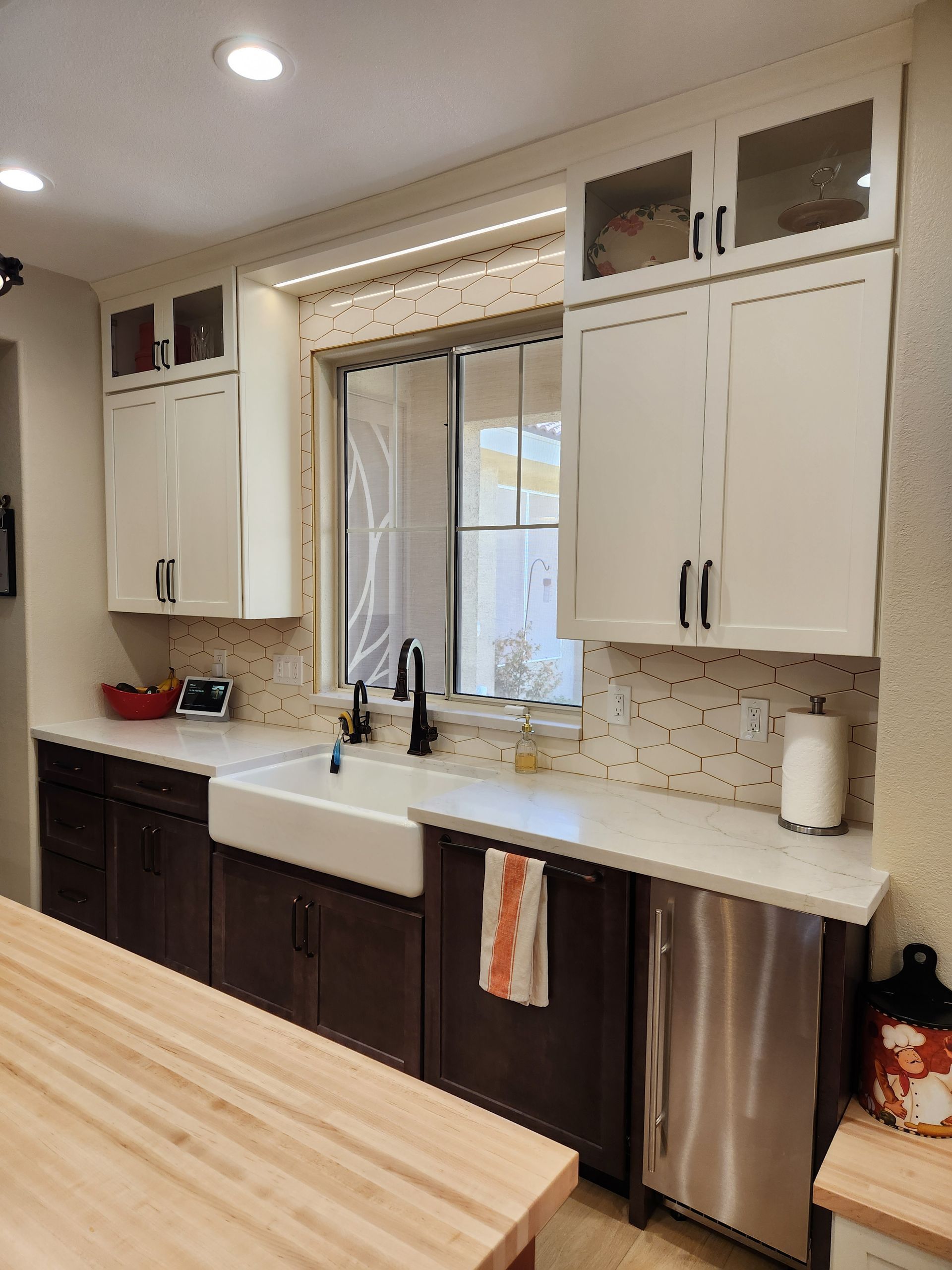Modern kitchen with white cabinets, dark lower cabinets, farmhouse sink, window, and butcher-block island countertop