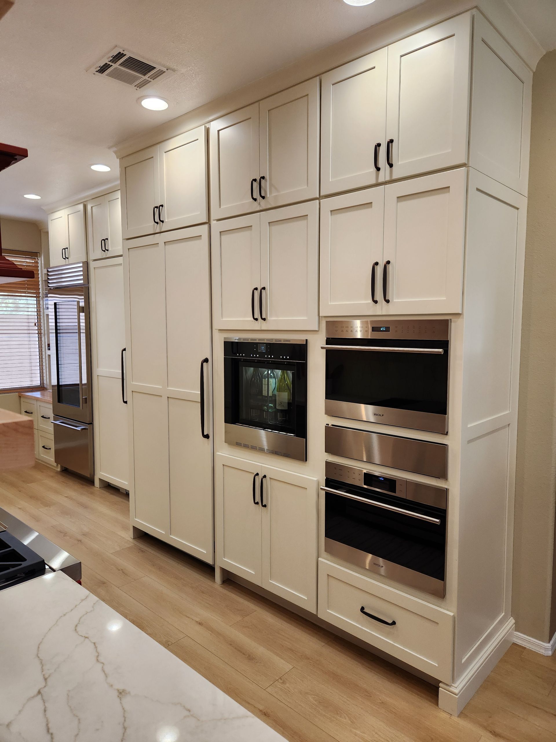 White built-in kitchen cabinets with a built-in oven and wine rack in a bright hallway-style kitchen.