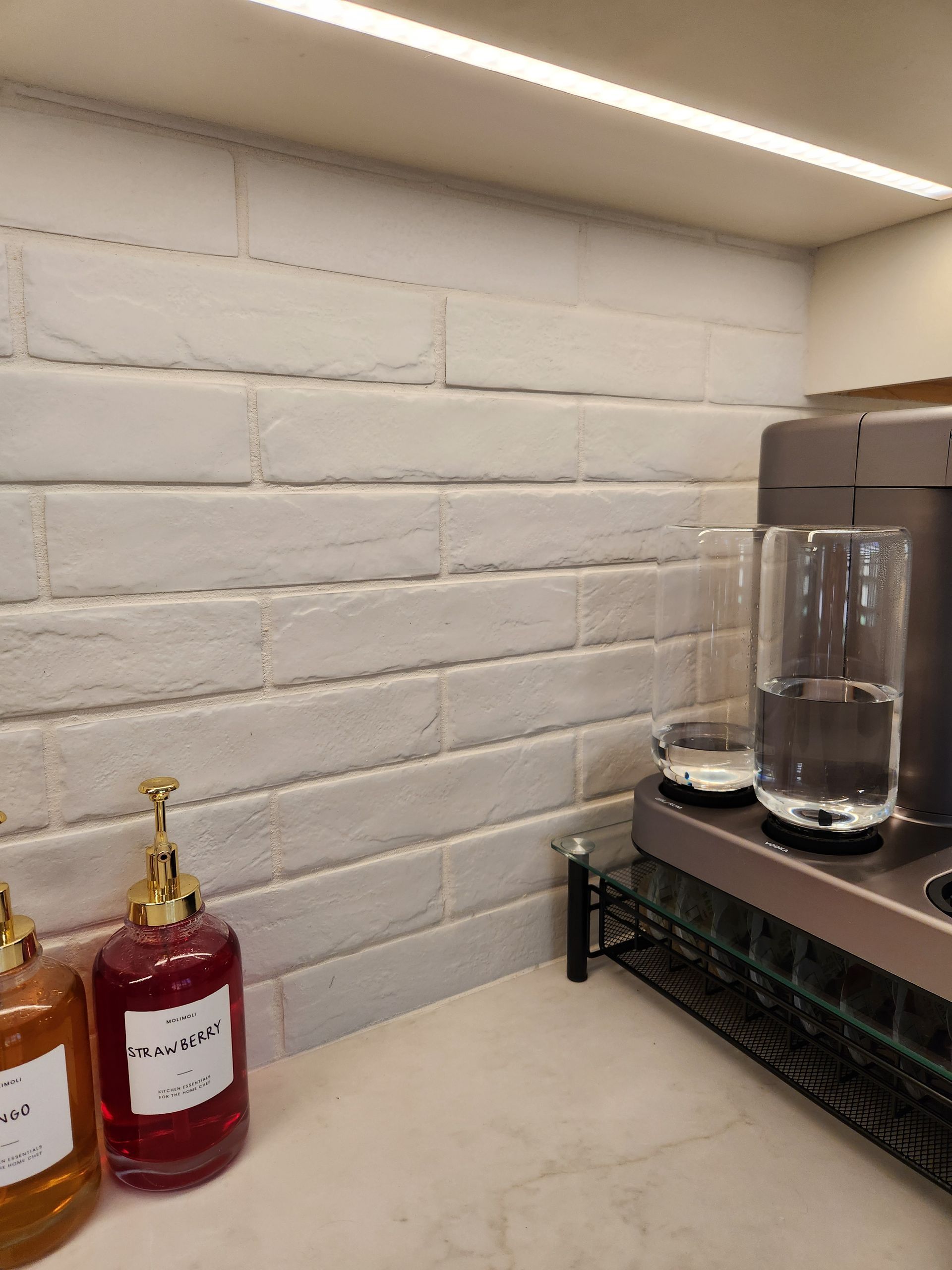 Kitchen counter with white brick backsplash, bottles on the left, and a glass container on the right