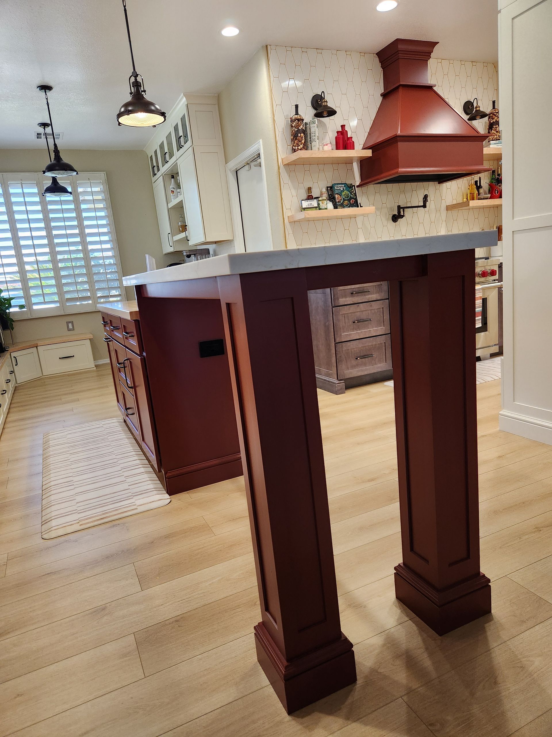 Modern kitchen with light wood floors, red range hood, island, and breakfast bar stools