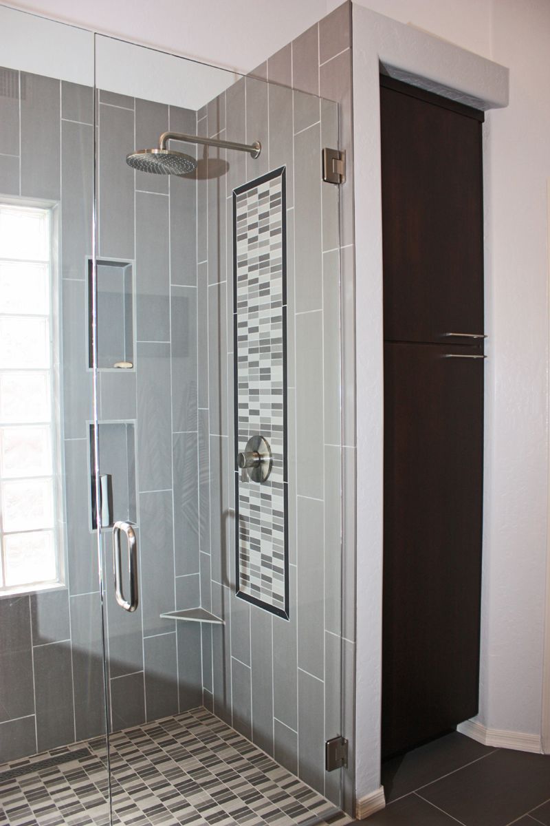 Glass shower stall with mosaic tile floor and wall, next to a dark doorway in a bathroom.