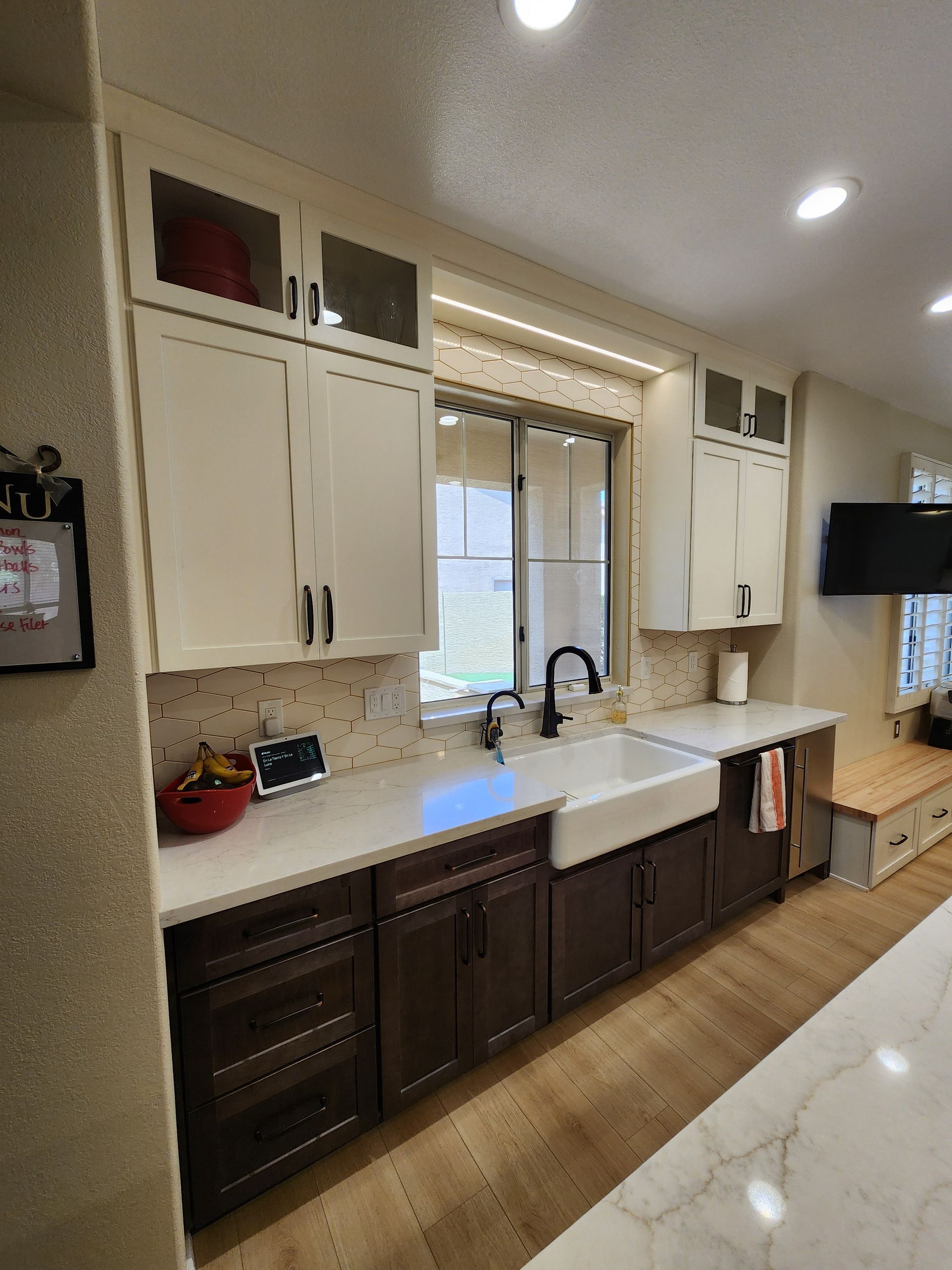 Bright kitchen with white cabinets, dark lower cabinets, farmhouse sink, and tiled backsplash.