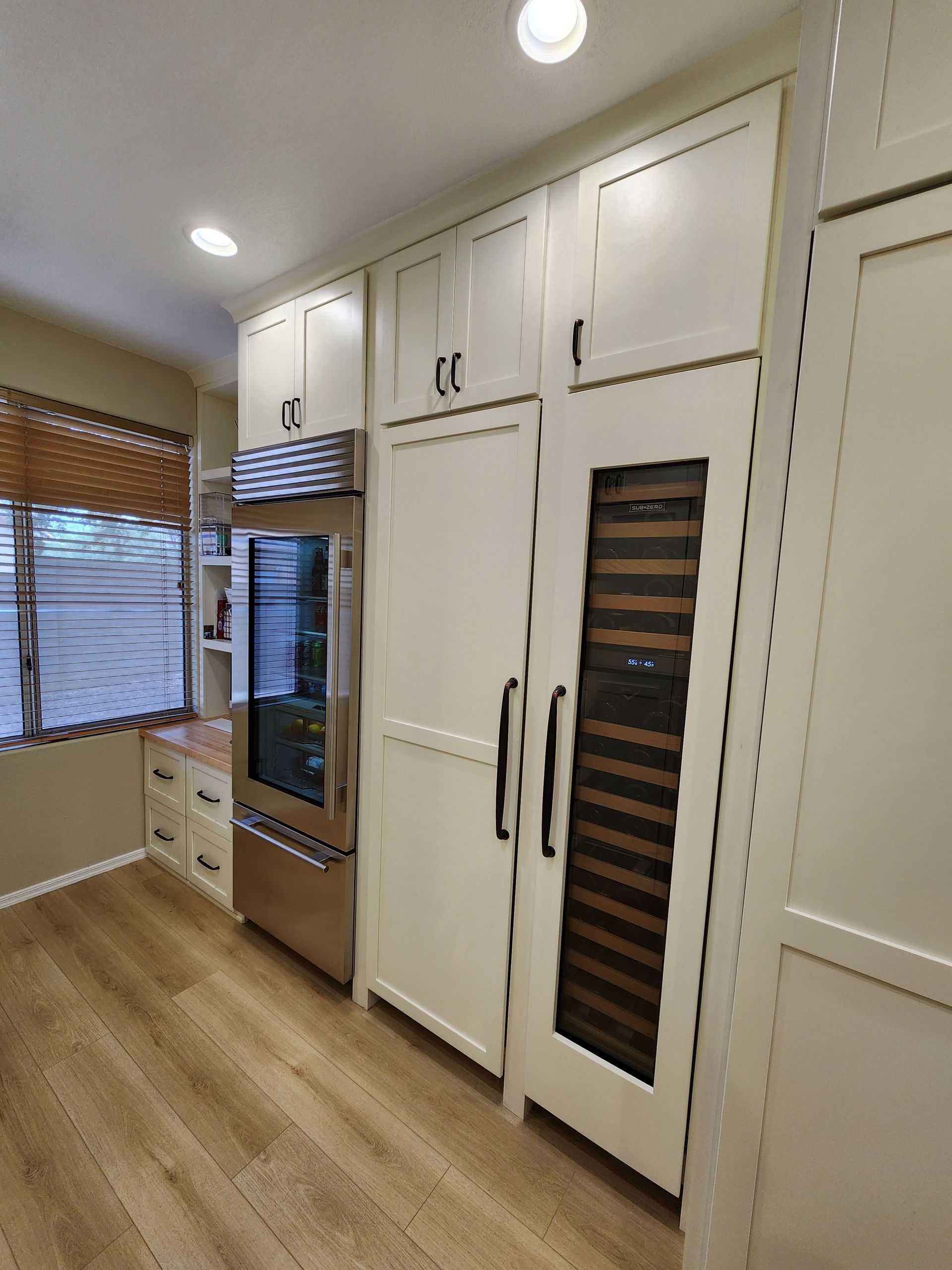 Bright kitchen with white cabinets, stainless oven, tall pantry, and wood floors.