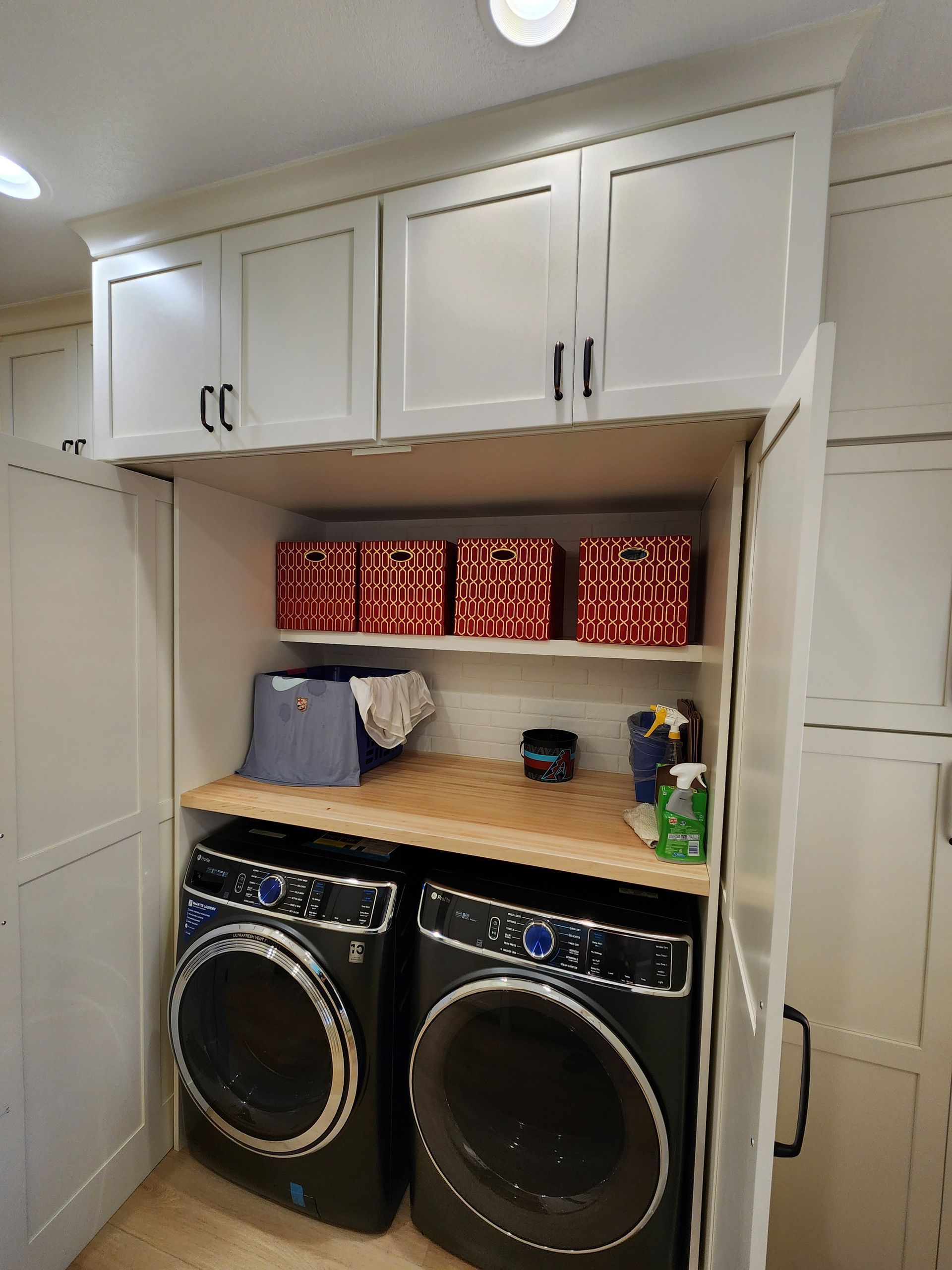 Laundry room with front-load washer and dryer, white cabinets, and shelf storage above.