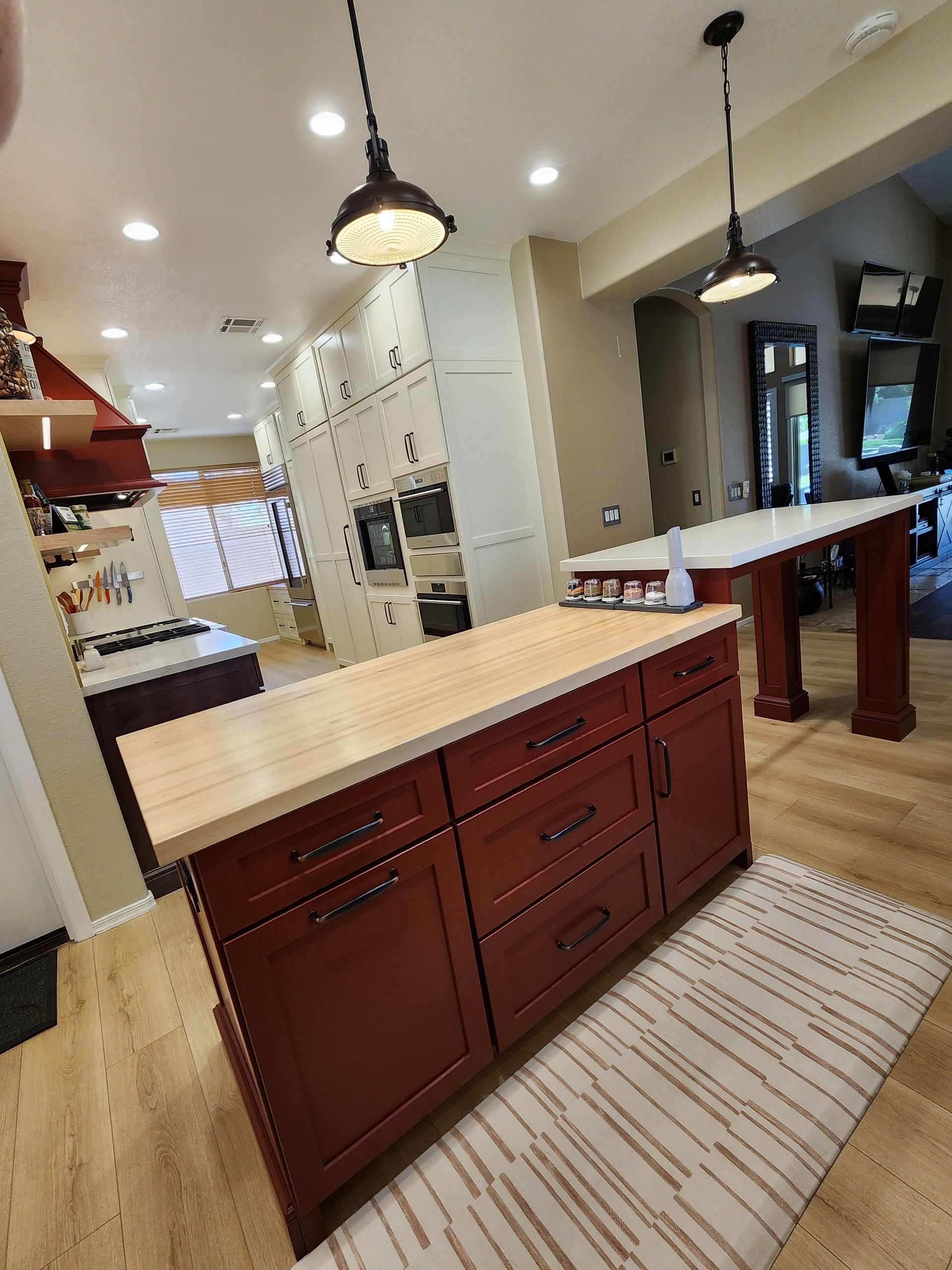 Kitchen with red island cabinets, light wood countertop, pendant lights, and a breakfast bar area