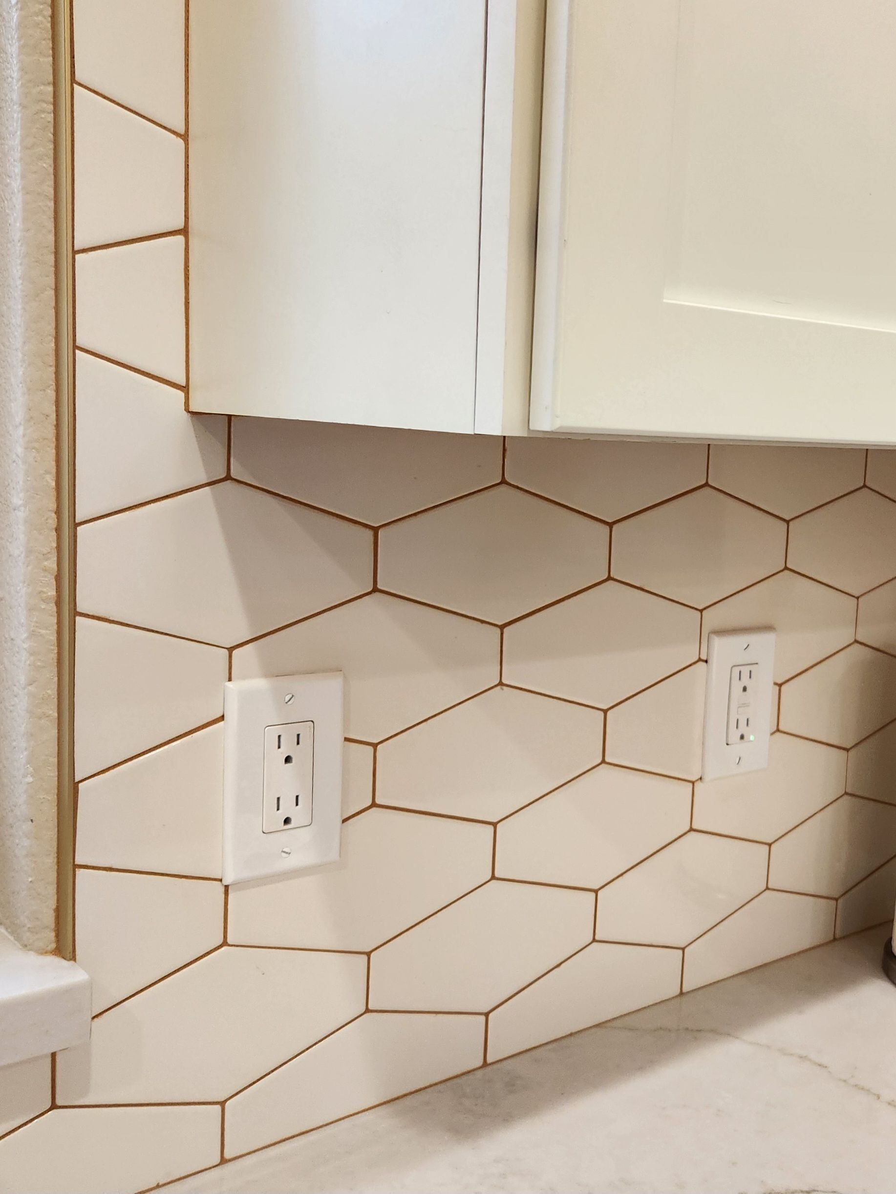 Kitchen backsplash with white geometric tile, two outlets, and a white cabinet above the counter
