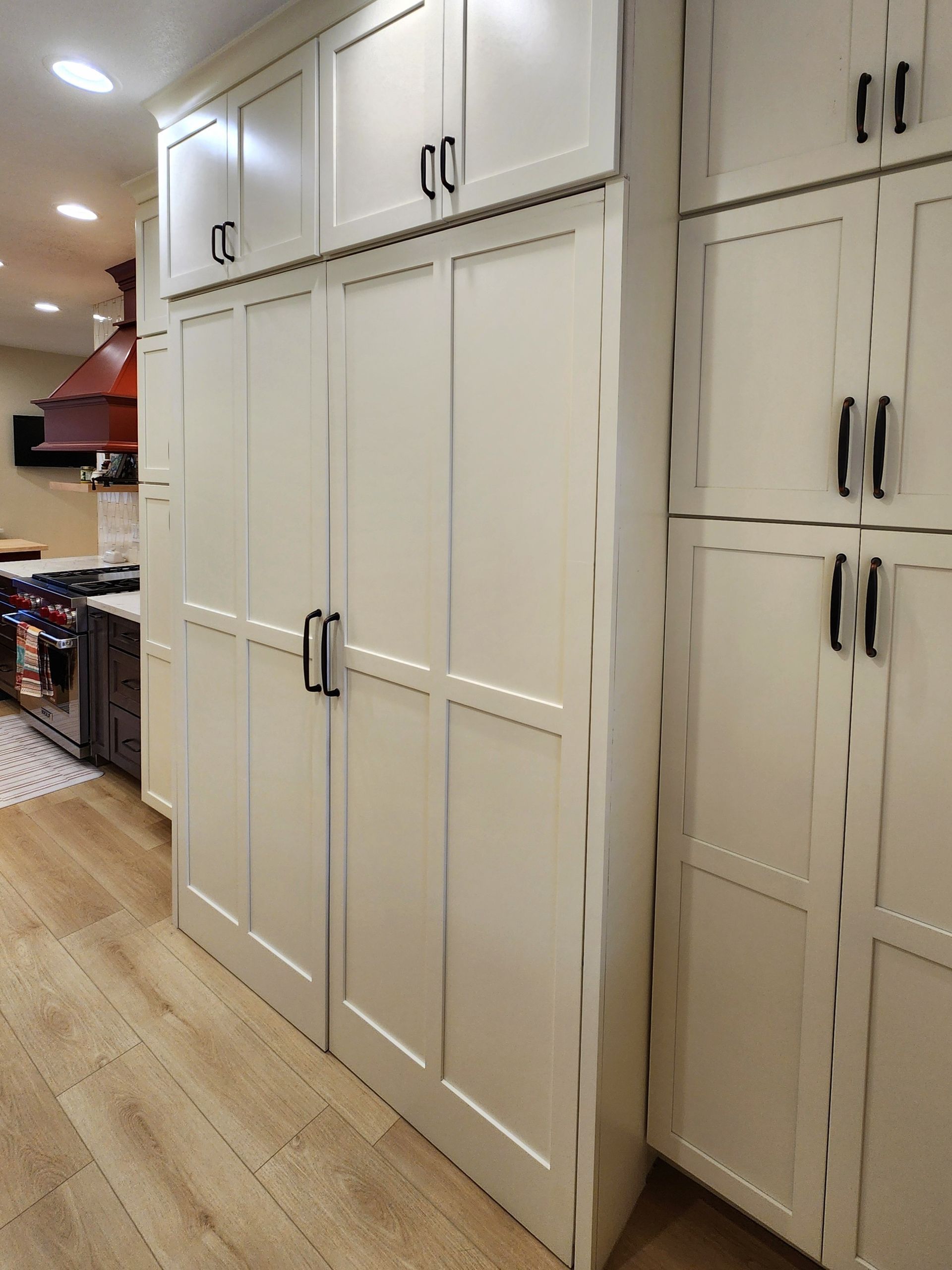 White built-in kitchen cabinets with black handles along a light wood floor in a home interior.