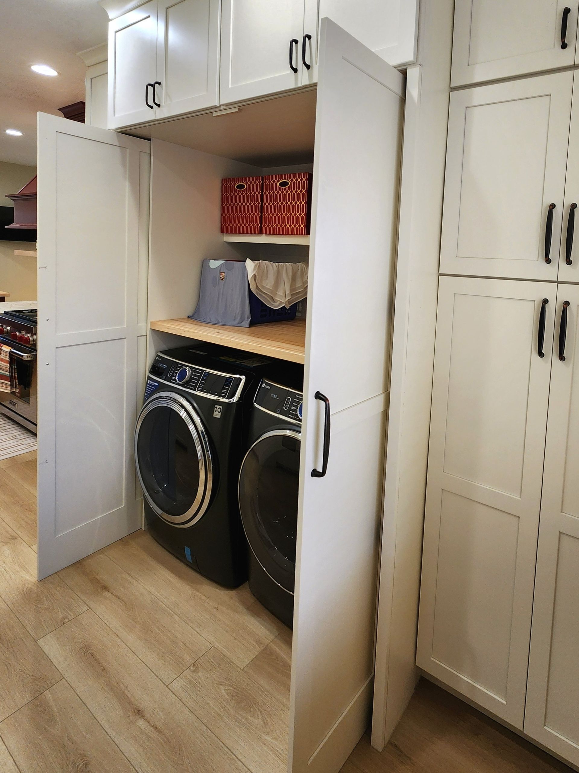 Laundry closet with stacked washer and dryer, open cabinet doors, and white storage shelves.