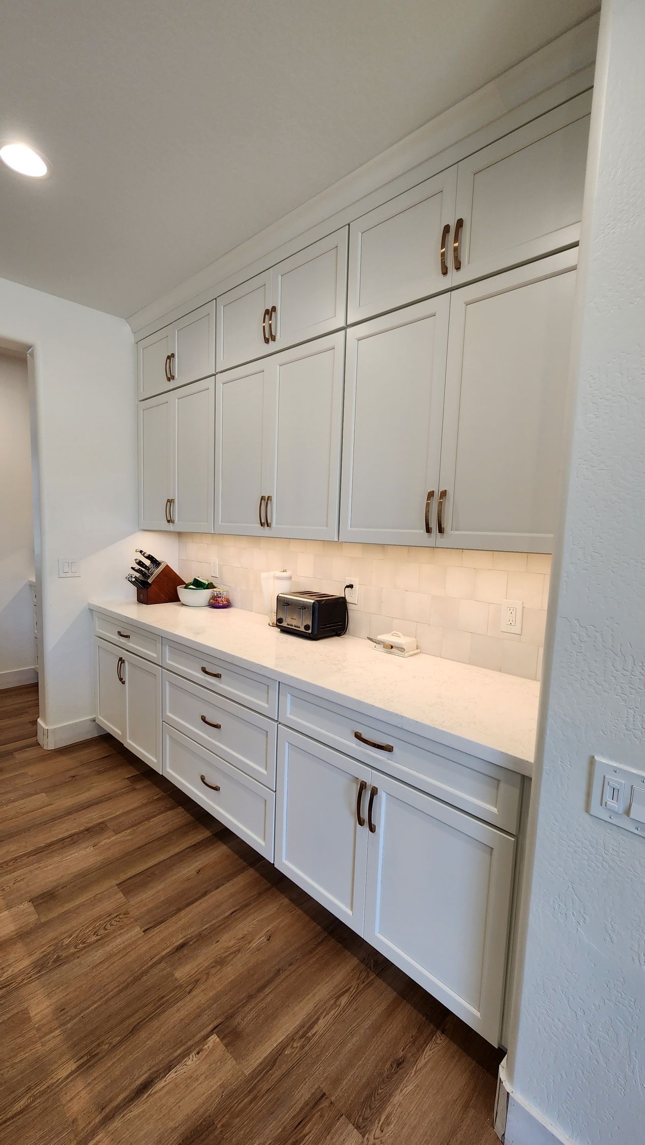 Bright white kitchen with tall cabinets, countertop appliances, and wood flooring.
