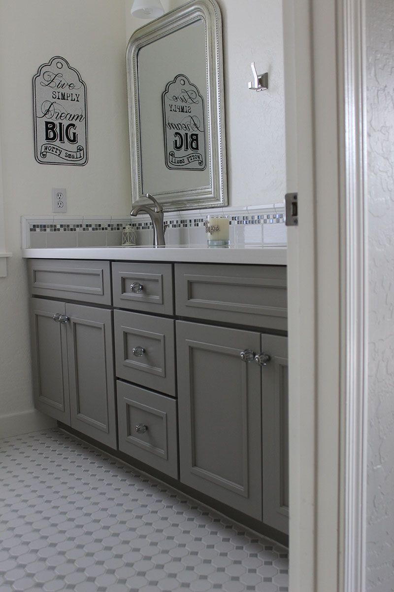 Gray bathroom vanity with double sinks, large mirrors, and patterned floor tiles