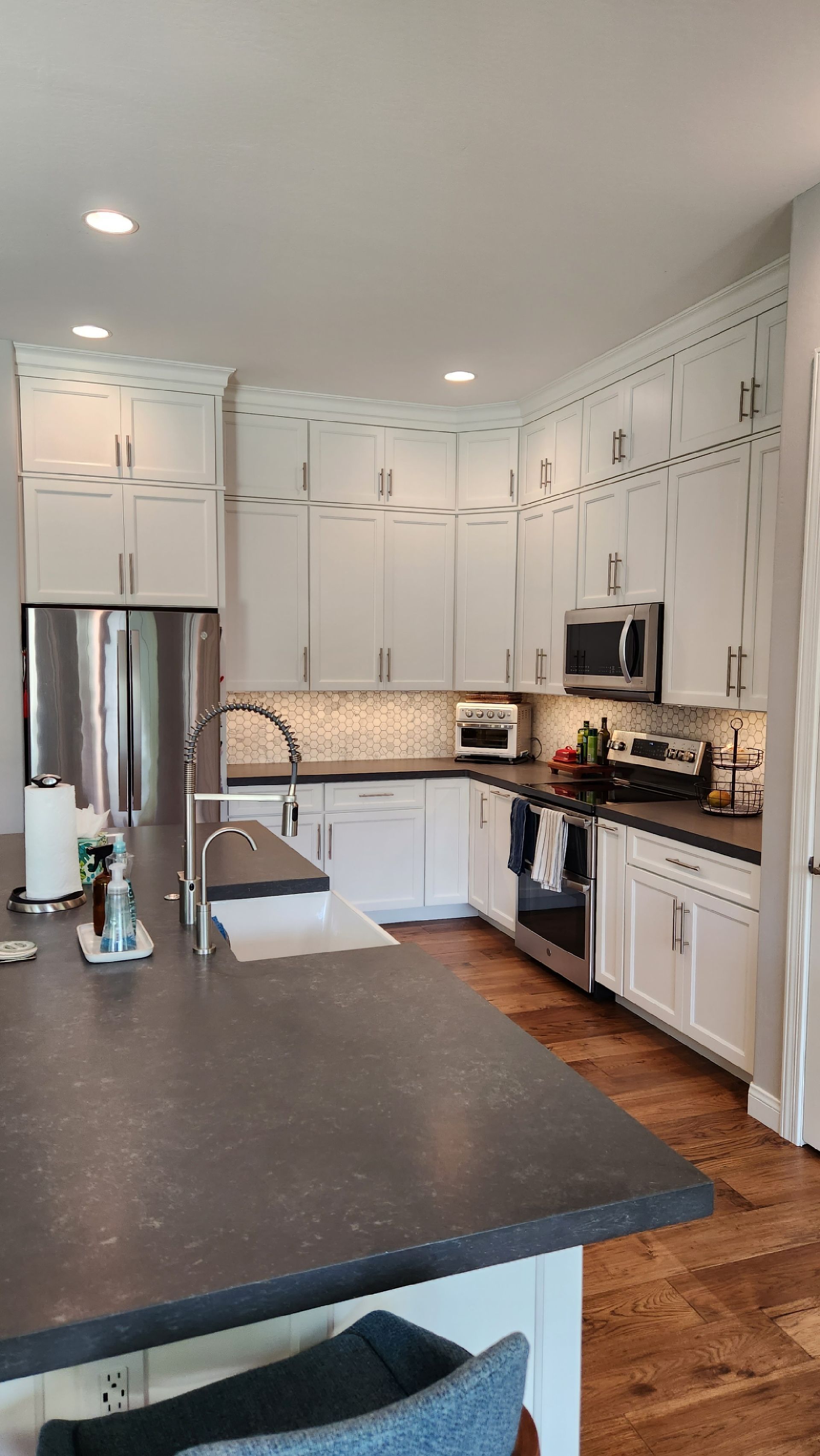 Bright white kitchen with dark island countertop, stainless fridge, and hardwood floors
