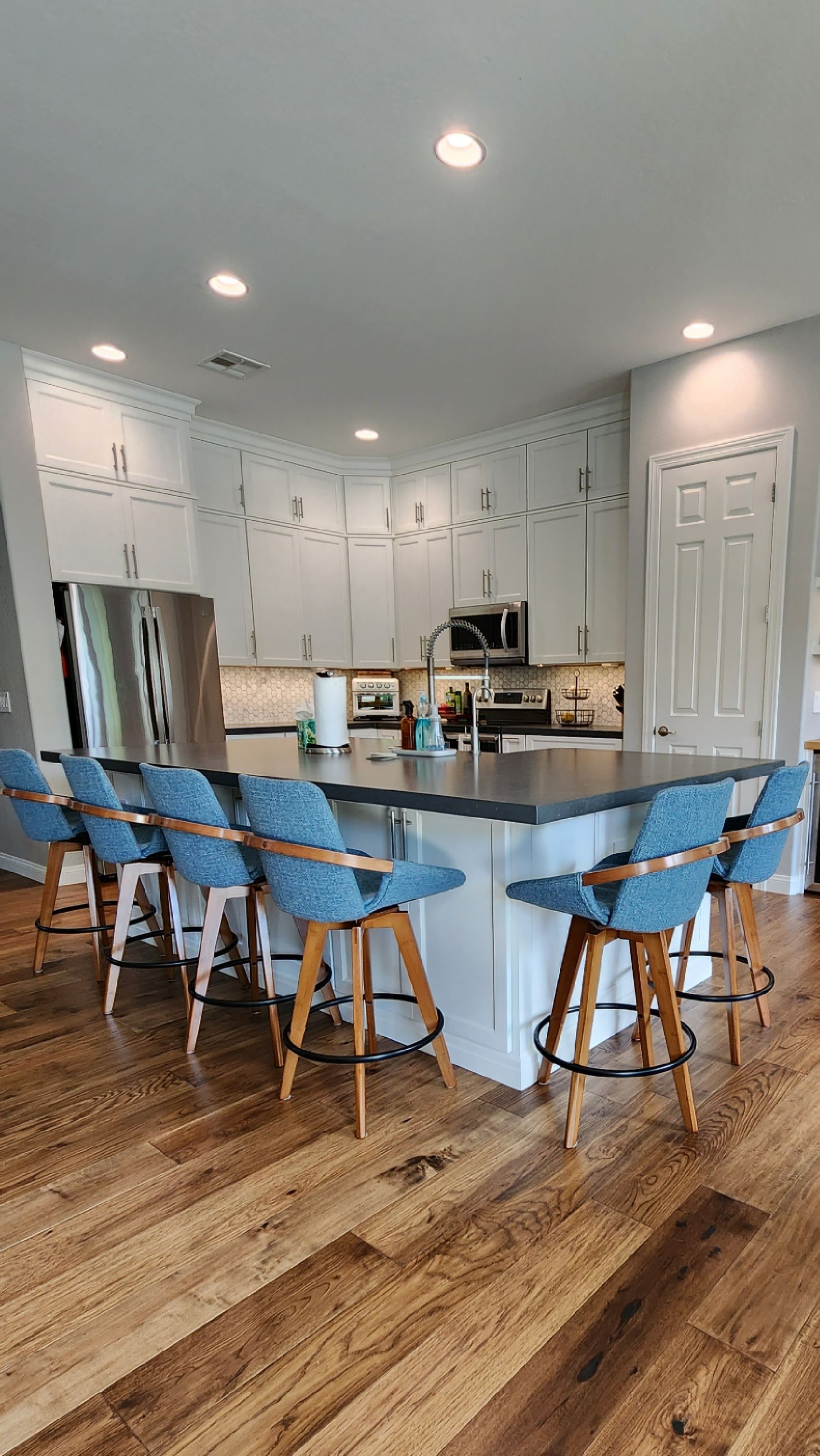 Bright kitchen with white cabinets, wood floors, and blue barstools around a central island.