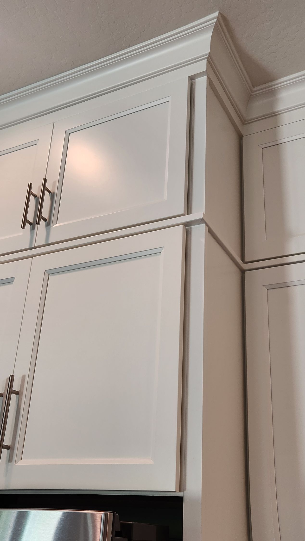 White kitchen cabinets with crown molding and metal handles, viewed from below.